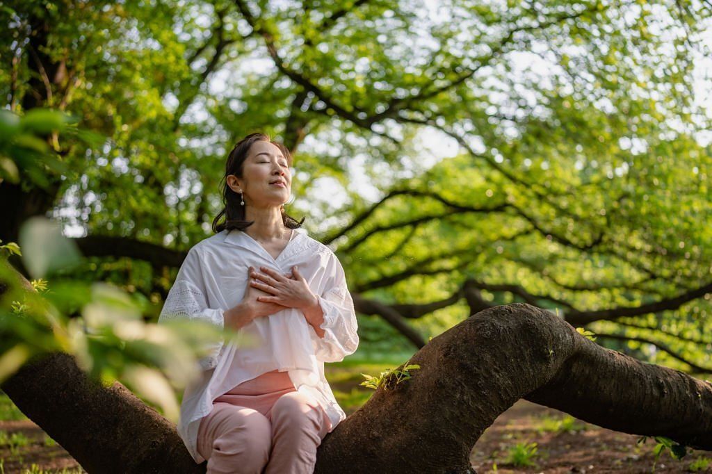 A woman is closing her eyes, doing breathing exercise and meditating in nature.