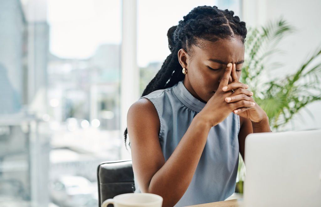 Stressed black businesswoman working on a laptop in an office alone(Image via Getty Images)