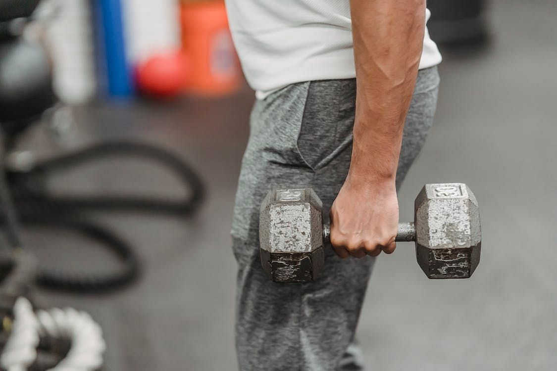To perform upright rows, stand with your feet shoulder-width apart and hold a barbell or dumbbells in front of your thighs (Julia Larson/ Pexels)