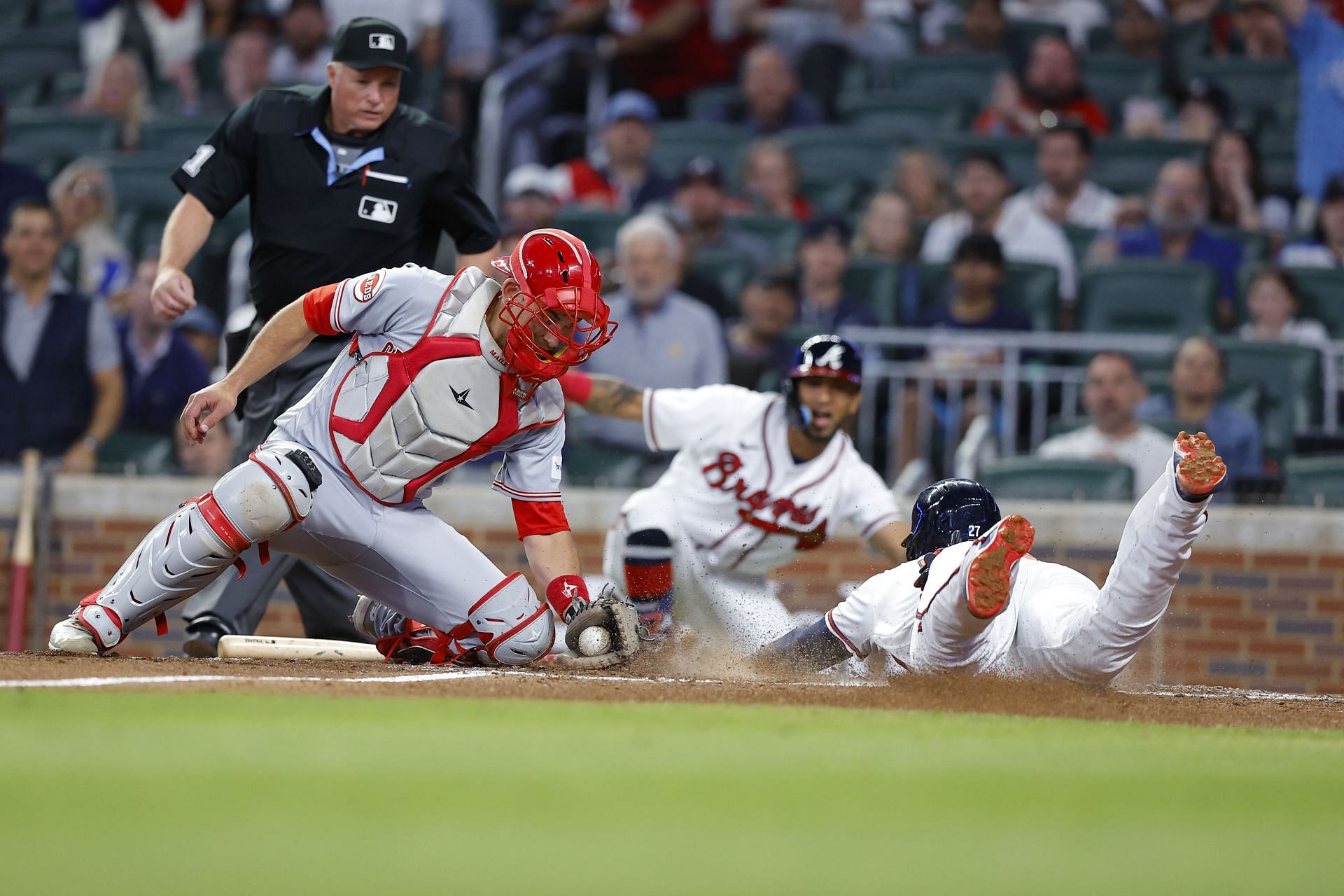 Austin Riley #27 of the Atlanta Braves slides in to score while beating the tag of Luke Maile #22 of the Cincinnati Reds