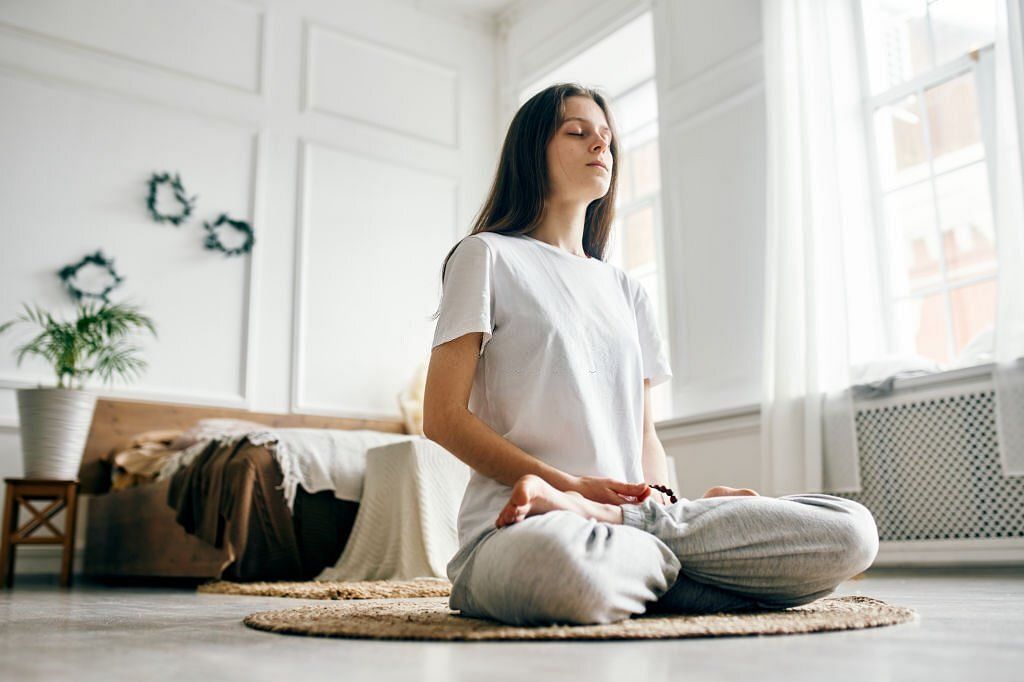 Full length of woman practicing breathing exercise. Young woman with eyes closed sitting in lotus position