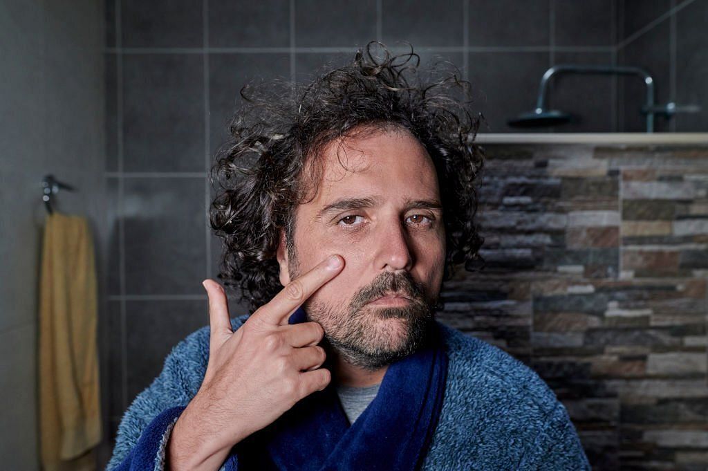 Man looking at dark circles in the bathroom mirror. (Image via Getty Images)