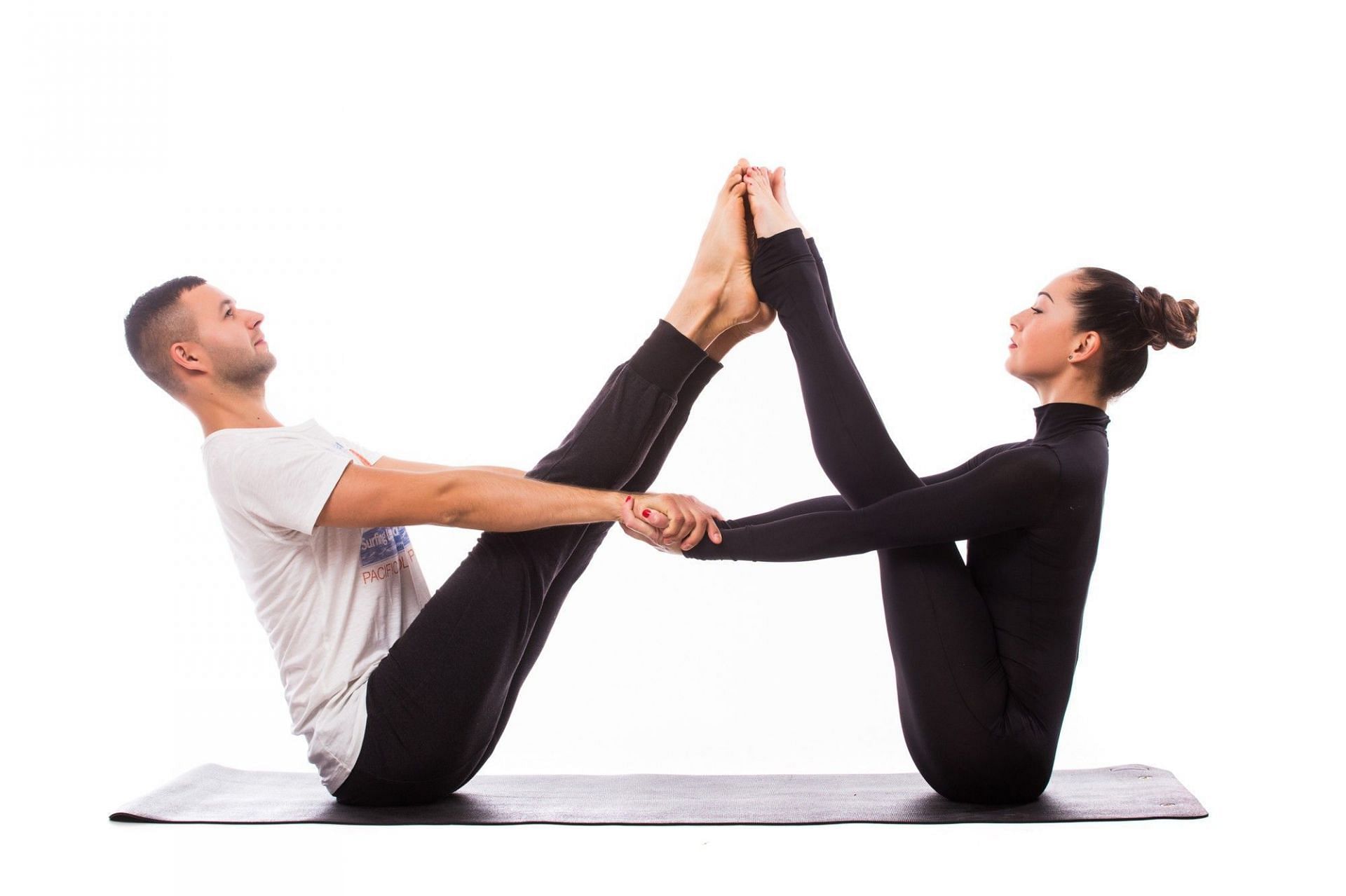 young Caucasian male and female couple practicing acrobatic yoga in a white  gym on mats. Loy HAND-TO-HAND, Skills Wind Mill, Position Type L-Bass,  Difficulty Really Hard, Number of Persons 2 Person Stock