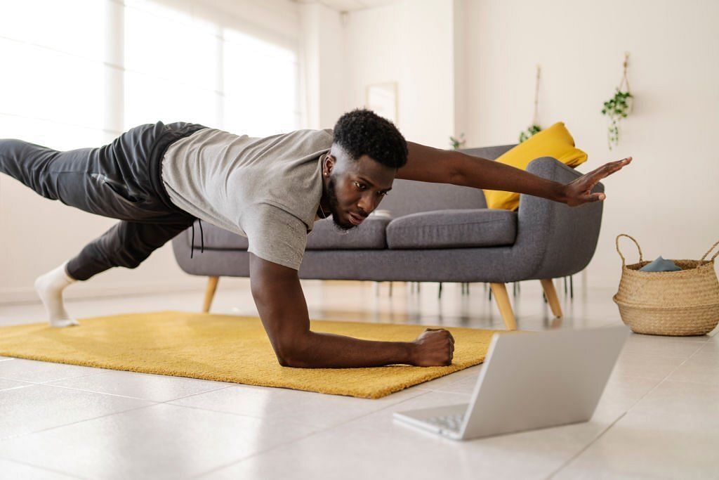 Man watching online exercise video on laptop while working out in the living room at home