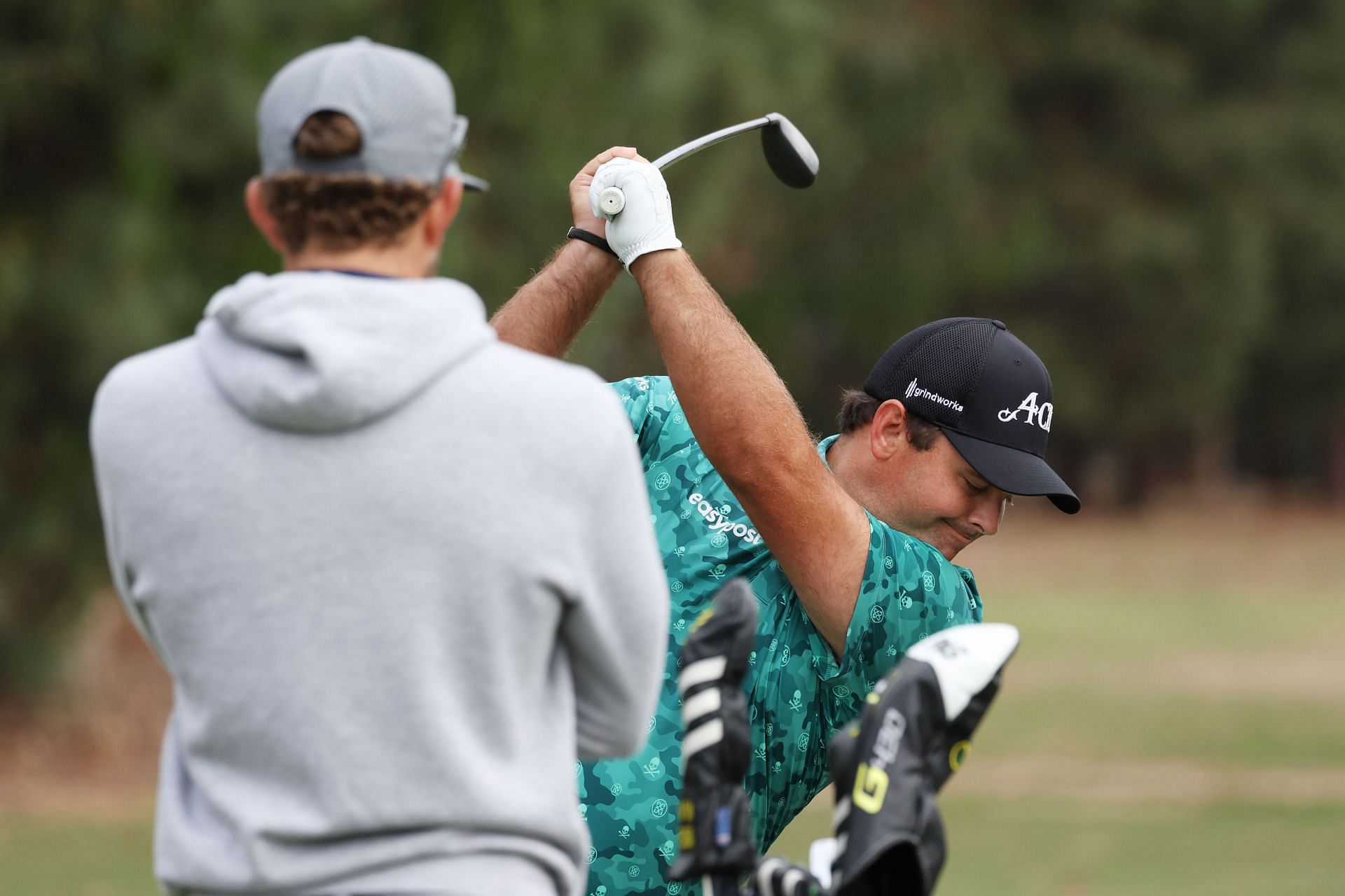 Patrick Reed hits on the range as his caddie Kessler Karain looks on during a practice round prior to the 123rd U.S. Open Championship at The Los Angeles Country Club