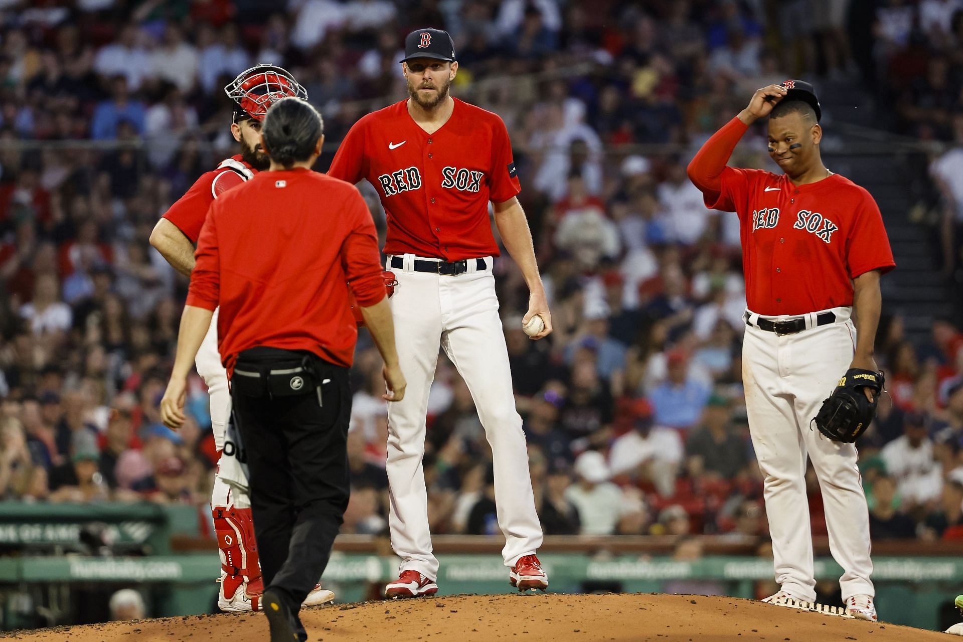 Chris Sale of the Boston Red Sox and teammate Rafael Devers, right, look on as a trainer comes to the mound to talk with Sale during the fourth inning against the Cincinnati Reds at Fenway Park on June 1.