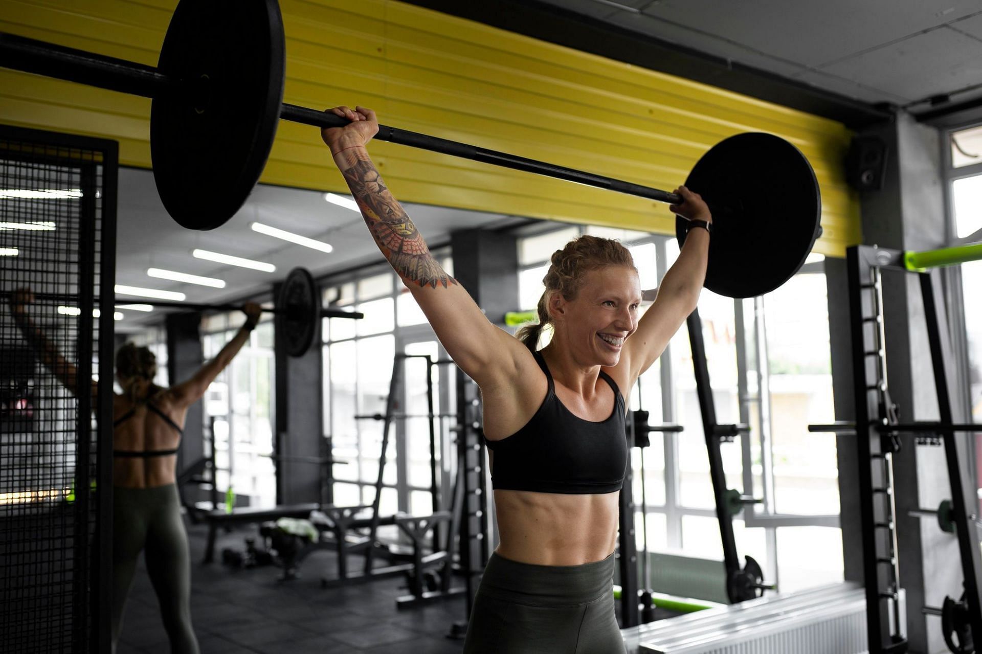 Overhead barbell press targets the upper back, shoulders, arms, and chest. (Image via Freepik)