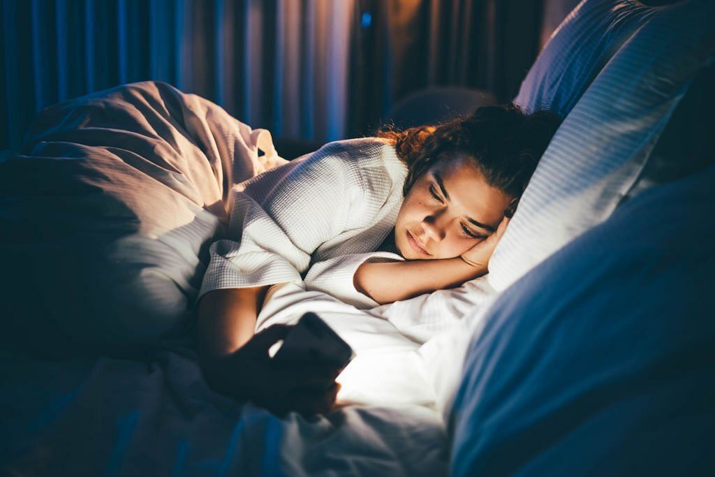 Young woman laying in bed and using smart phone(Image via Getty Images)