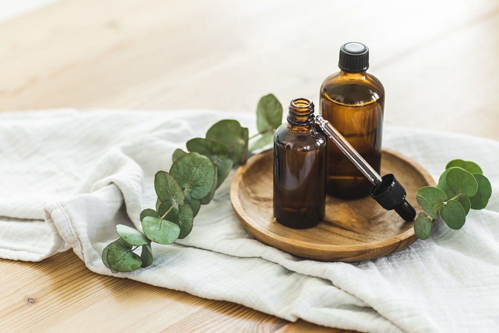 Various amber glass bottles for cosmetics, natural organic medicine, essential oils or other liquids on wooden plate near muslin textile and eucalyptus(Image via Getty Images)