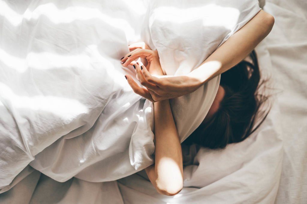 Sleepless Woman Lying In Bed Hiding Under Duvet(Image via Getty Images)