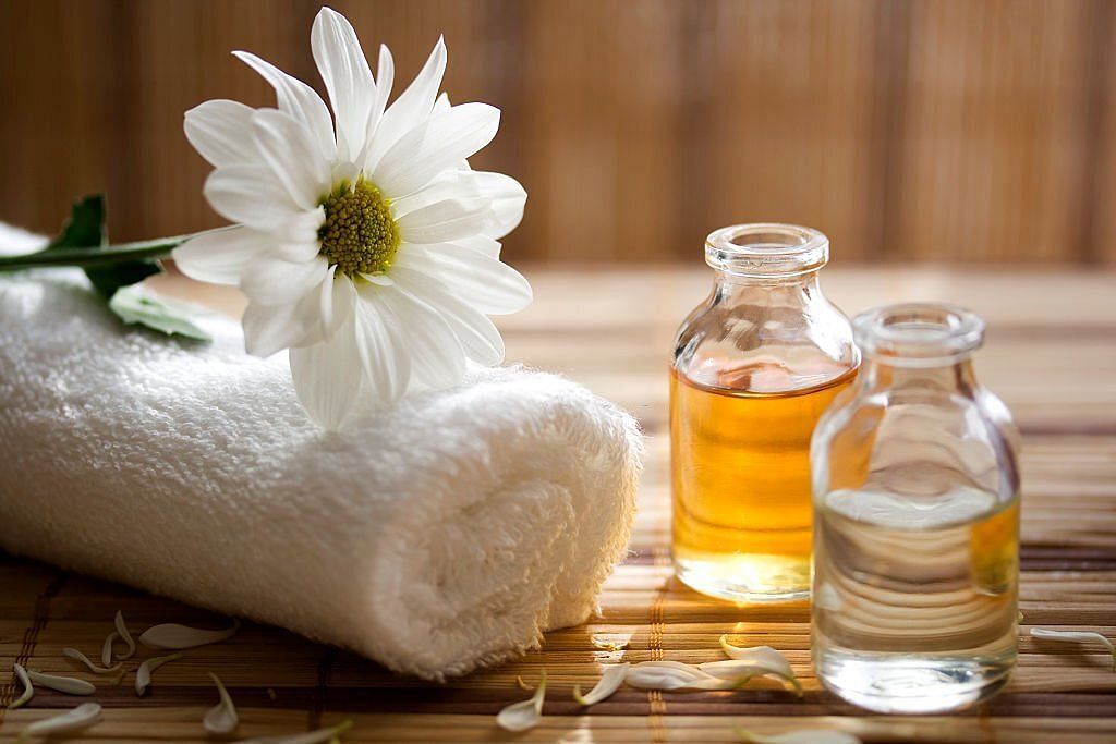 Aroma therapy oils placed next to a white towel and flower(Image via Getty Images)