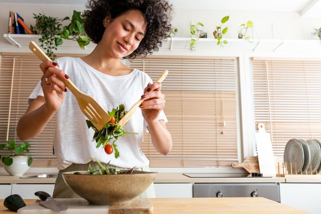Happy young multiracial woman mixing bowl of fresh salad. Copy space.Healthy lifestyle concept(Image via Getty Images)