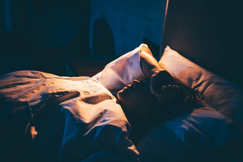 Woman with Insomnia. Young woman lying on bed with hand on forehead(Image via Getty Images)