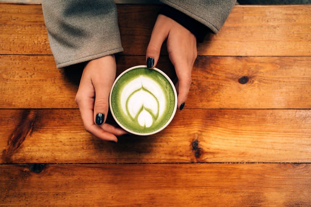 Woman hands hold a ceramic cup with matcha green tea latte