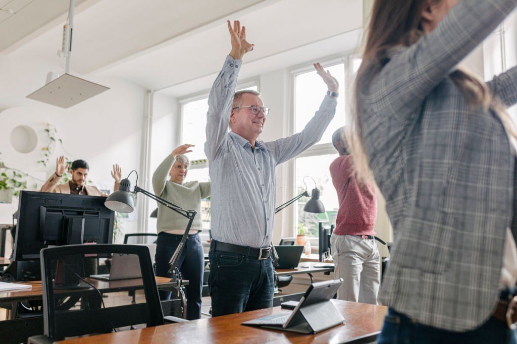 A group of office workers taking part in a stretching exercise by their desks together(Image via Getty Images)