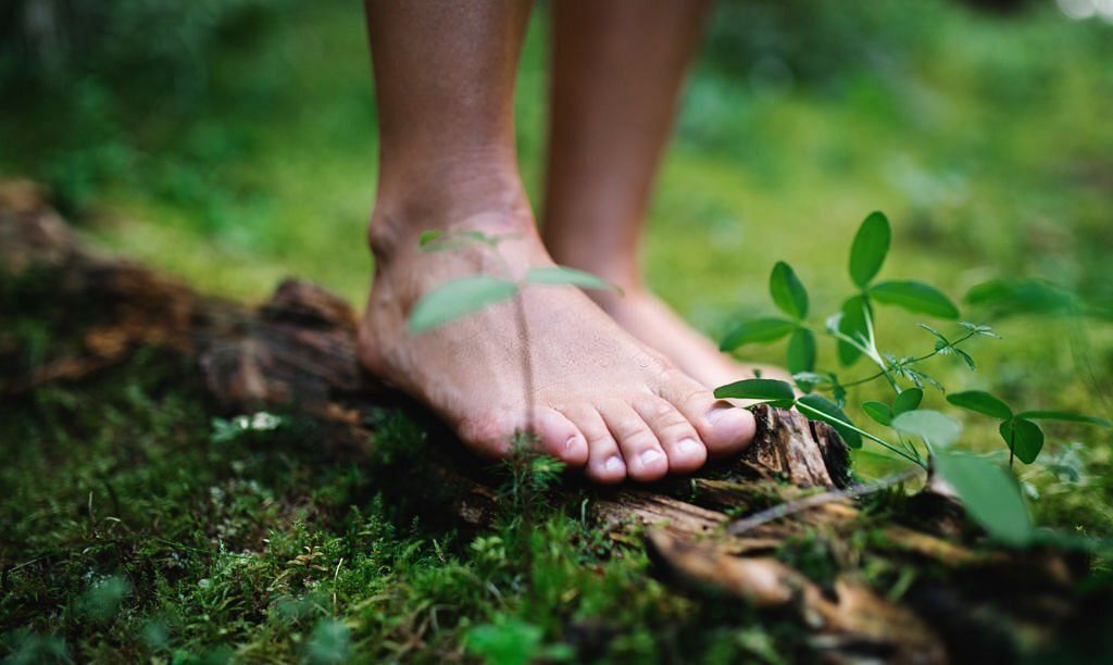 Bare feet of man standing barefoot outdoors in nature, grounding and forest bathing concept(Image via Getty Images)