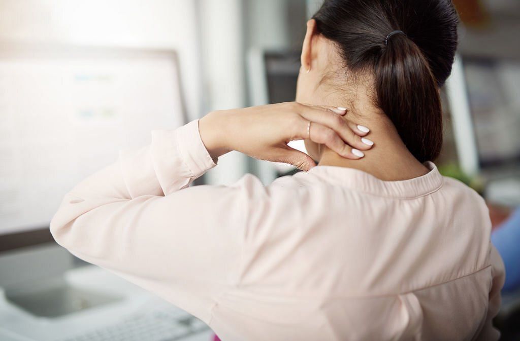 Rearview shot of a young businesswoman experiencing neck pain while working at her desk in a modern office