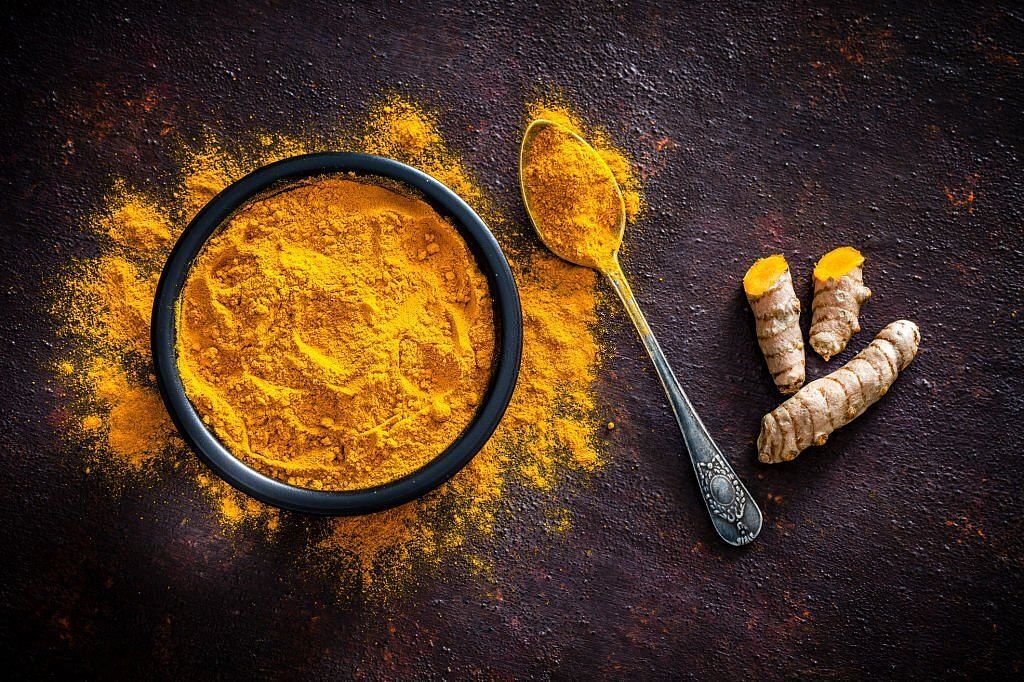 Top view of a black bowl filled with turmeric powder shot on abstract brown rustic table(Image via Getty Images)