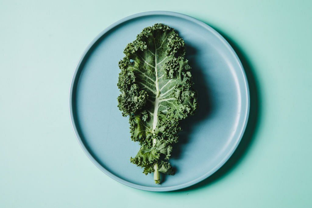 overhead view of kale on a plate against green background(Image via Getty Images)