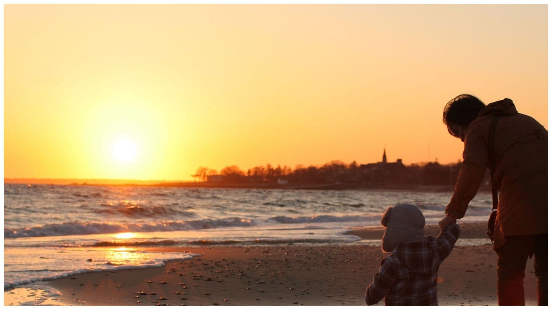 A child and mother walking on the beach. (Image via Getty Images)