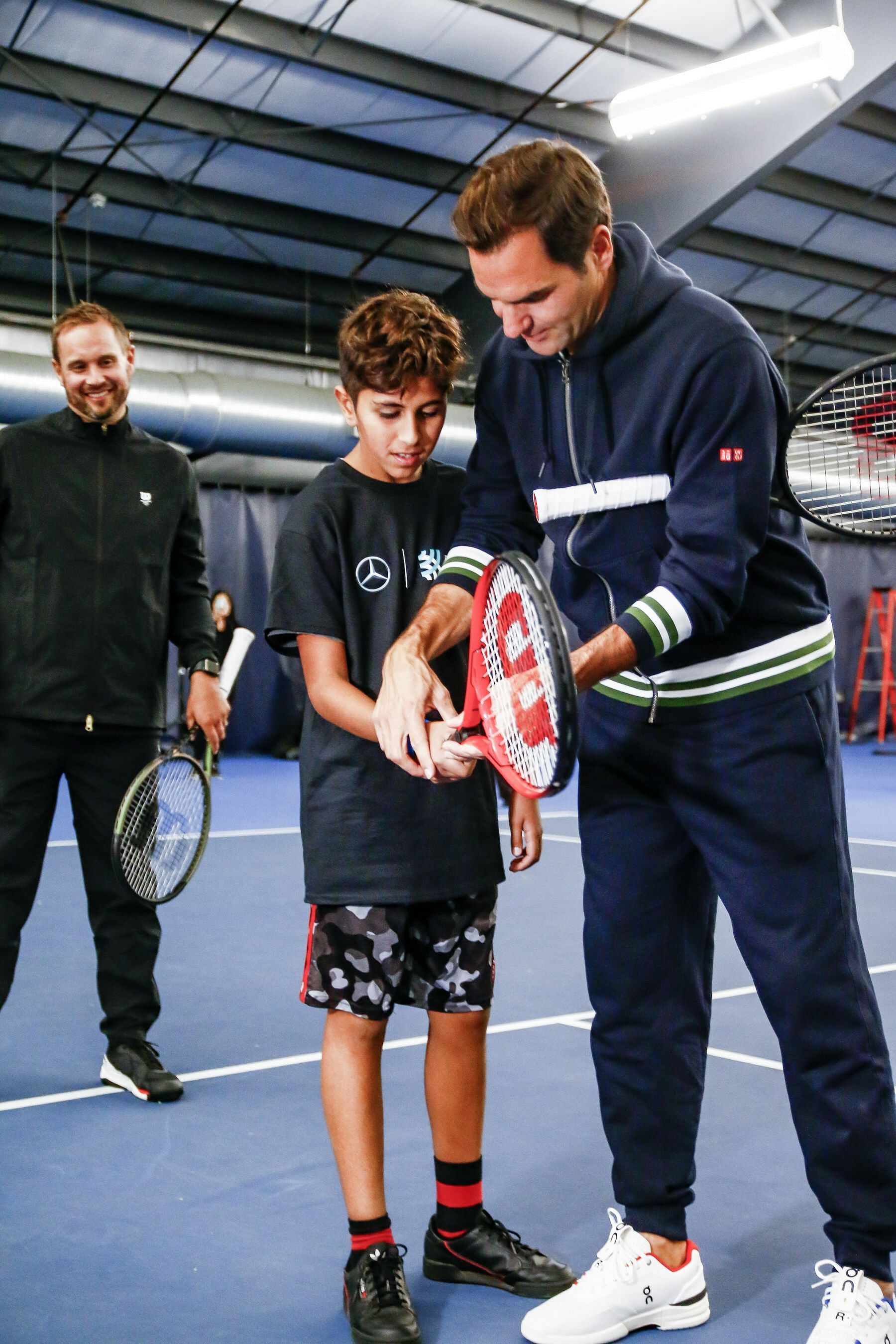 The Swiss maestro helps a young volunteer adjust his racket grip