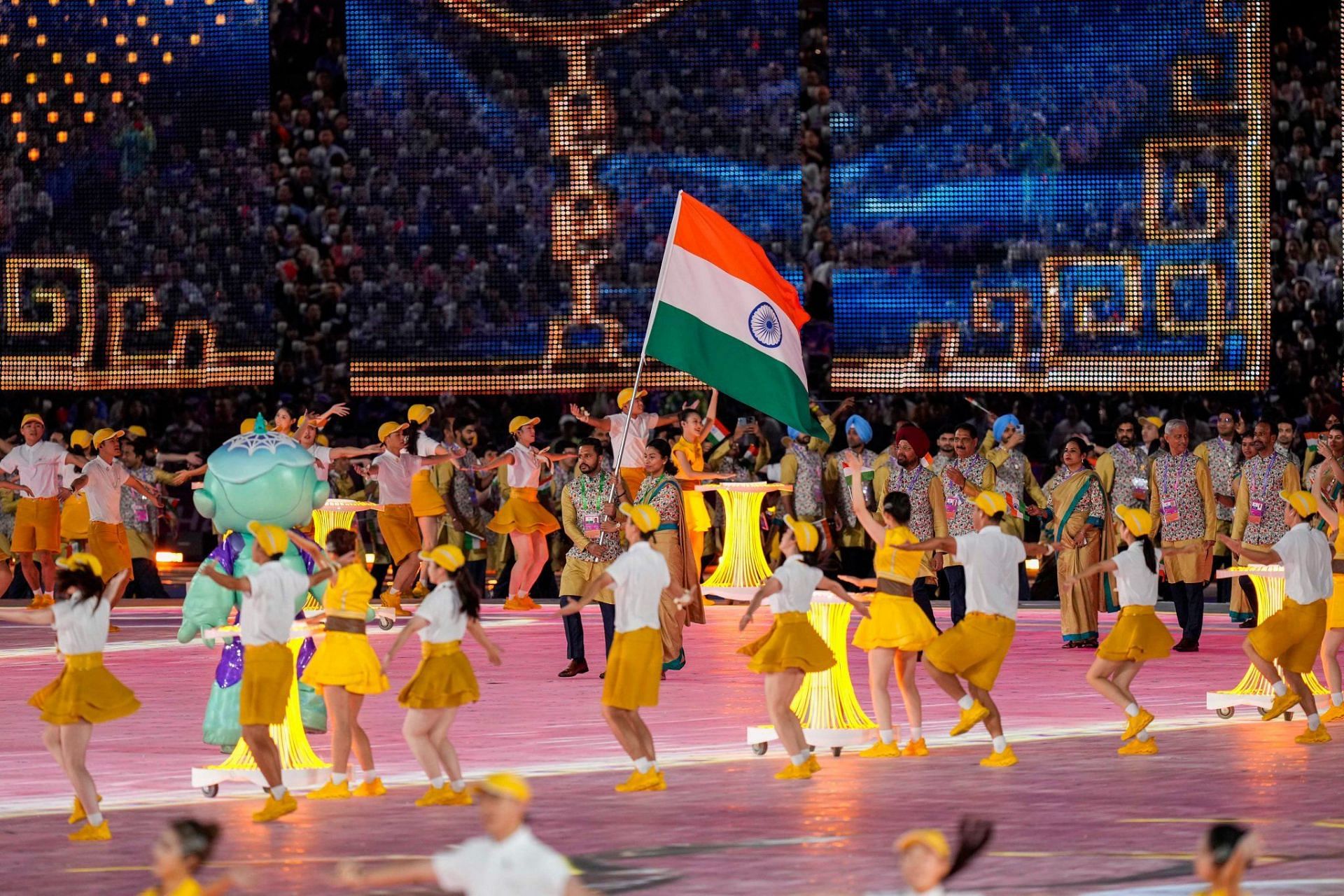 चीनी कलाकारों के बीच भारतीय ध्वज को थामे चलते हरमनप्रीत सिंह और लोवलीना।