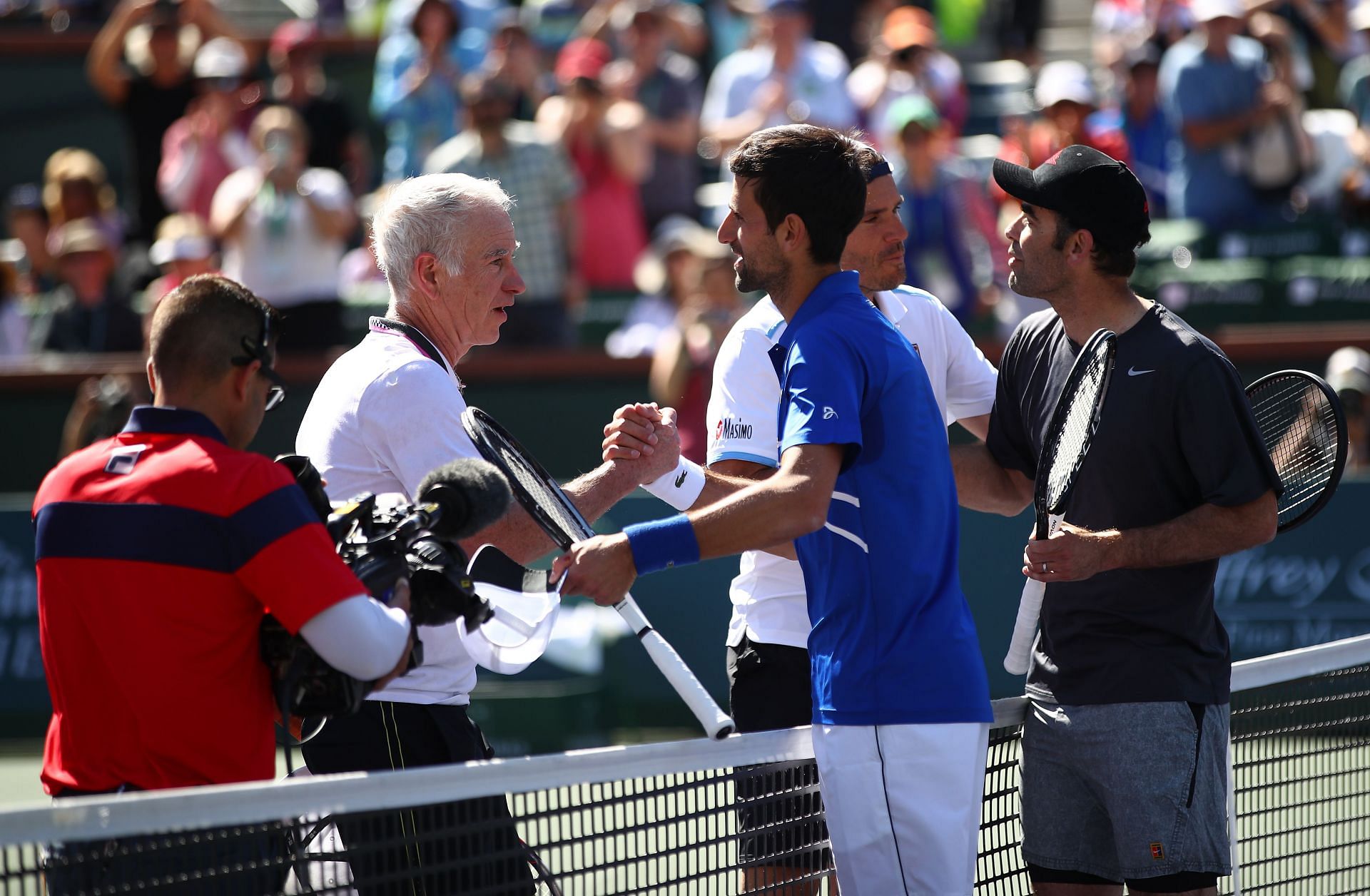 John McEnroe (in white) shakes hands with Novak Djokovic (in blue) in an exhibition match at the 2023 Indian Wells.