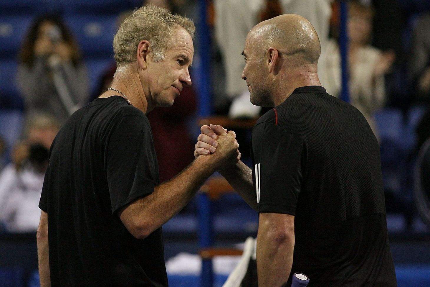 Andre Agassi and John McEnroe greet each other at the net