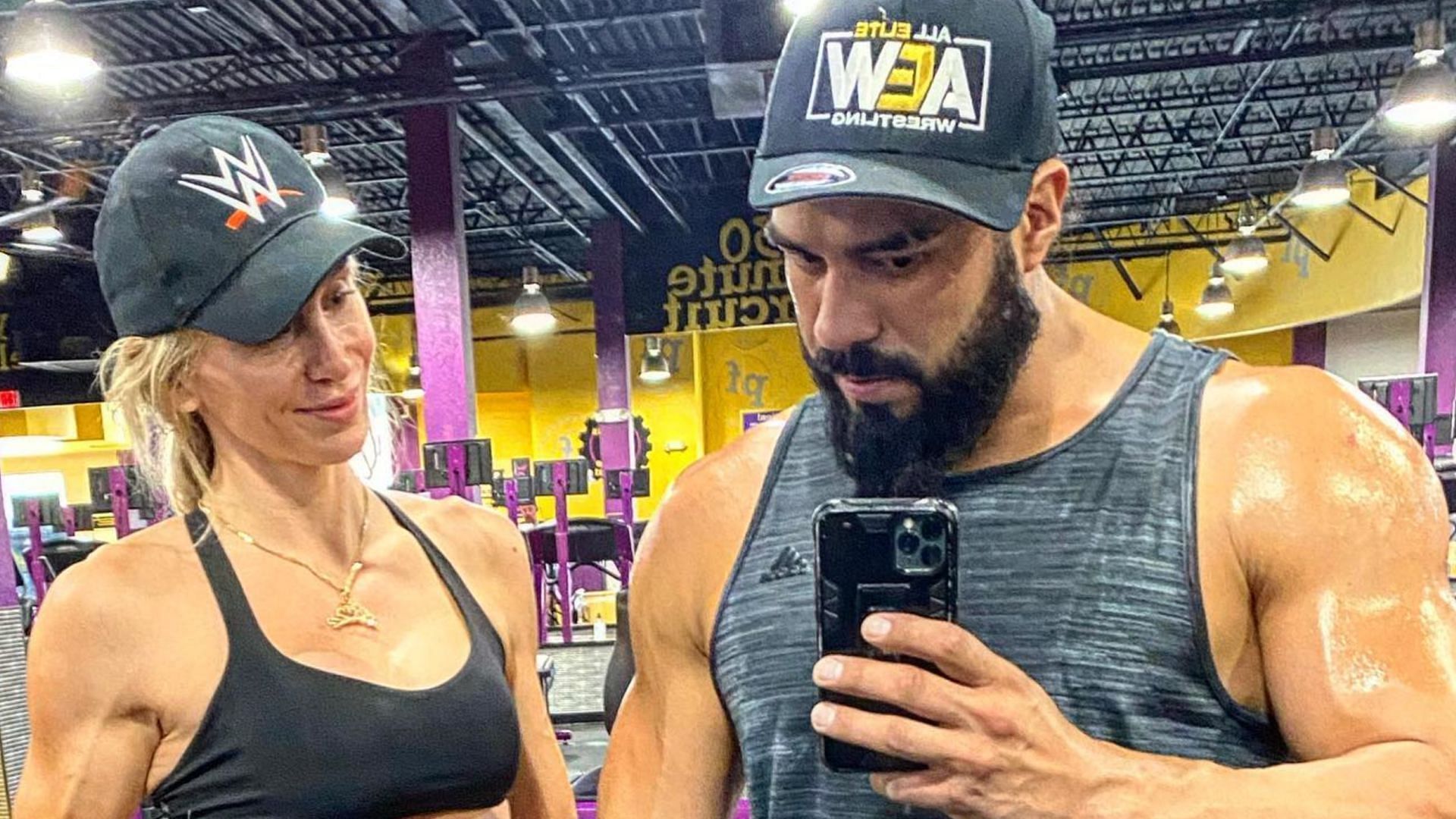 Charlotte Flair wears her WWE hat at the gym, Andrade wears his AEW hat at the gym