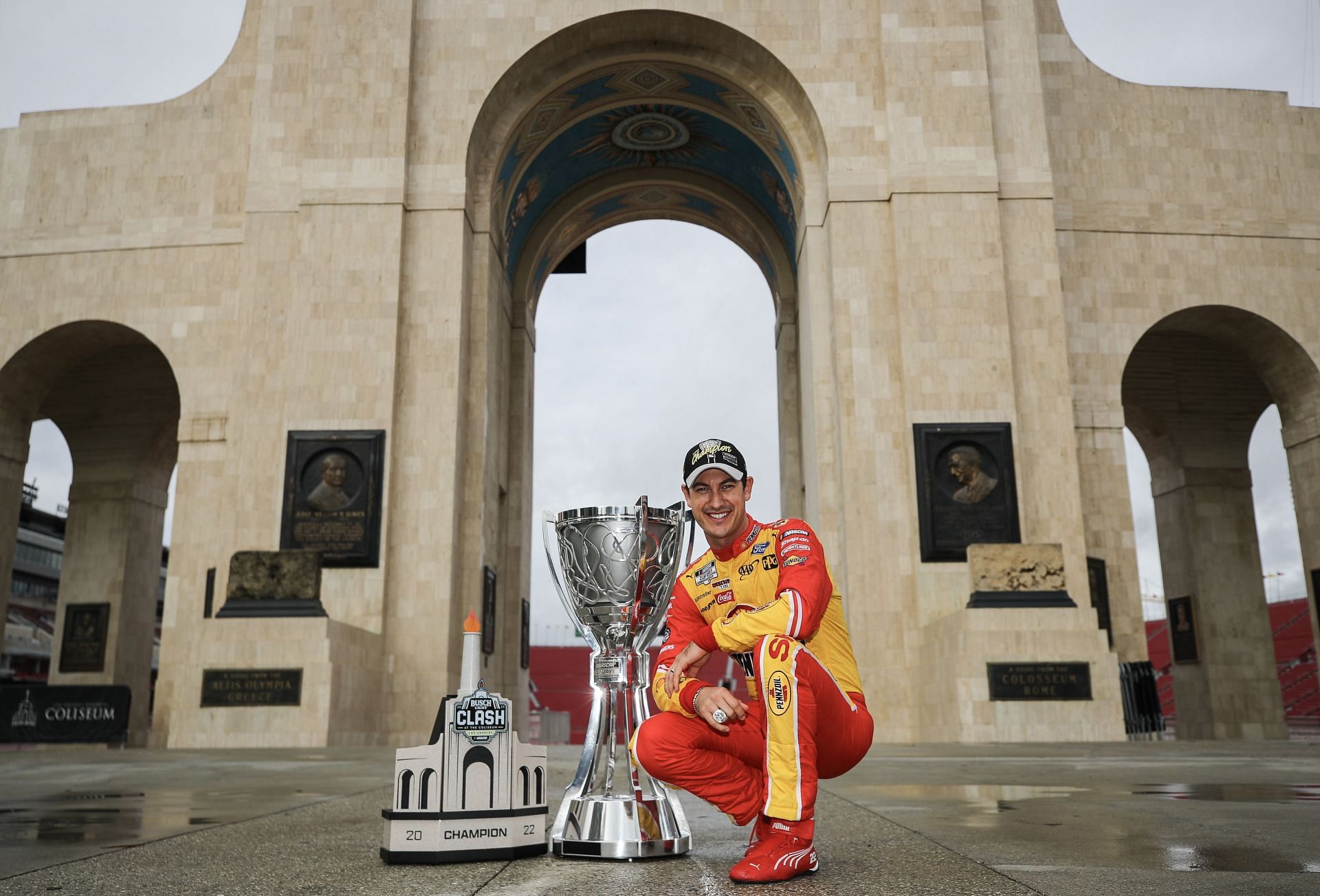 Joey Logano poses with his 2022 NASCAR Cup Series Championship trophy and his 2022 NASCAR Clash at the Coliseum trophy