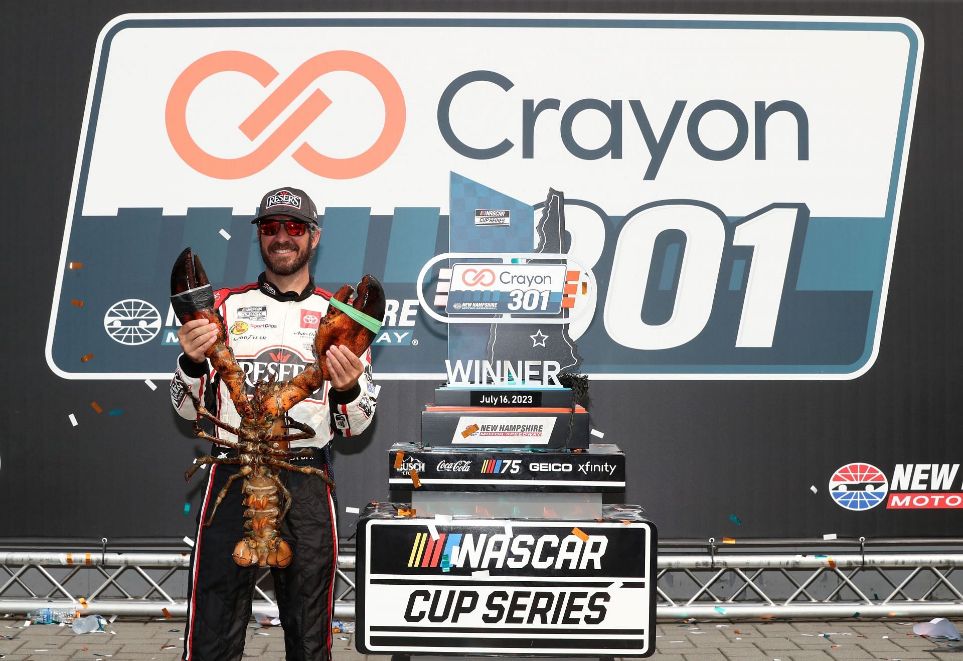 Martin Truex Jr. poses with Loudon the Lobster in victory lane after winning the NASCAR Cup Series Crayon 301. Courtesy: Getty Christopher Bell celebrates in victory lane after winning the NASCAR Cup Series Ambetter 301. Courtesy: Getty.