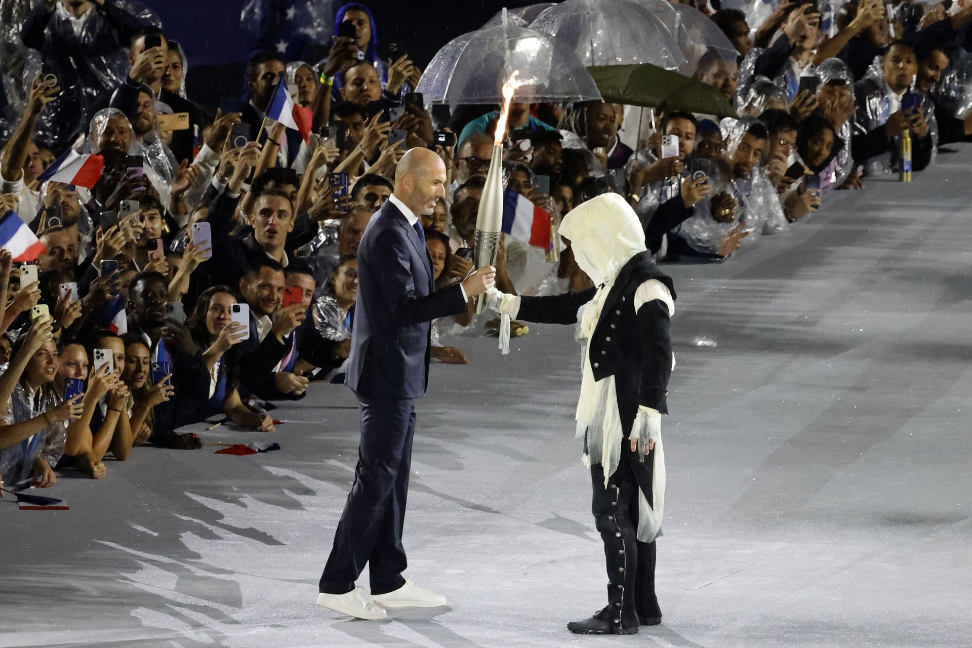 The hooded guy handing over the Olympic flame to Zinedine Zidane at the opening ceremony of Paris Olympics [Image Source: Getty]