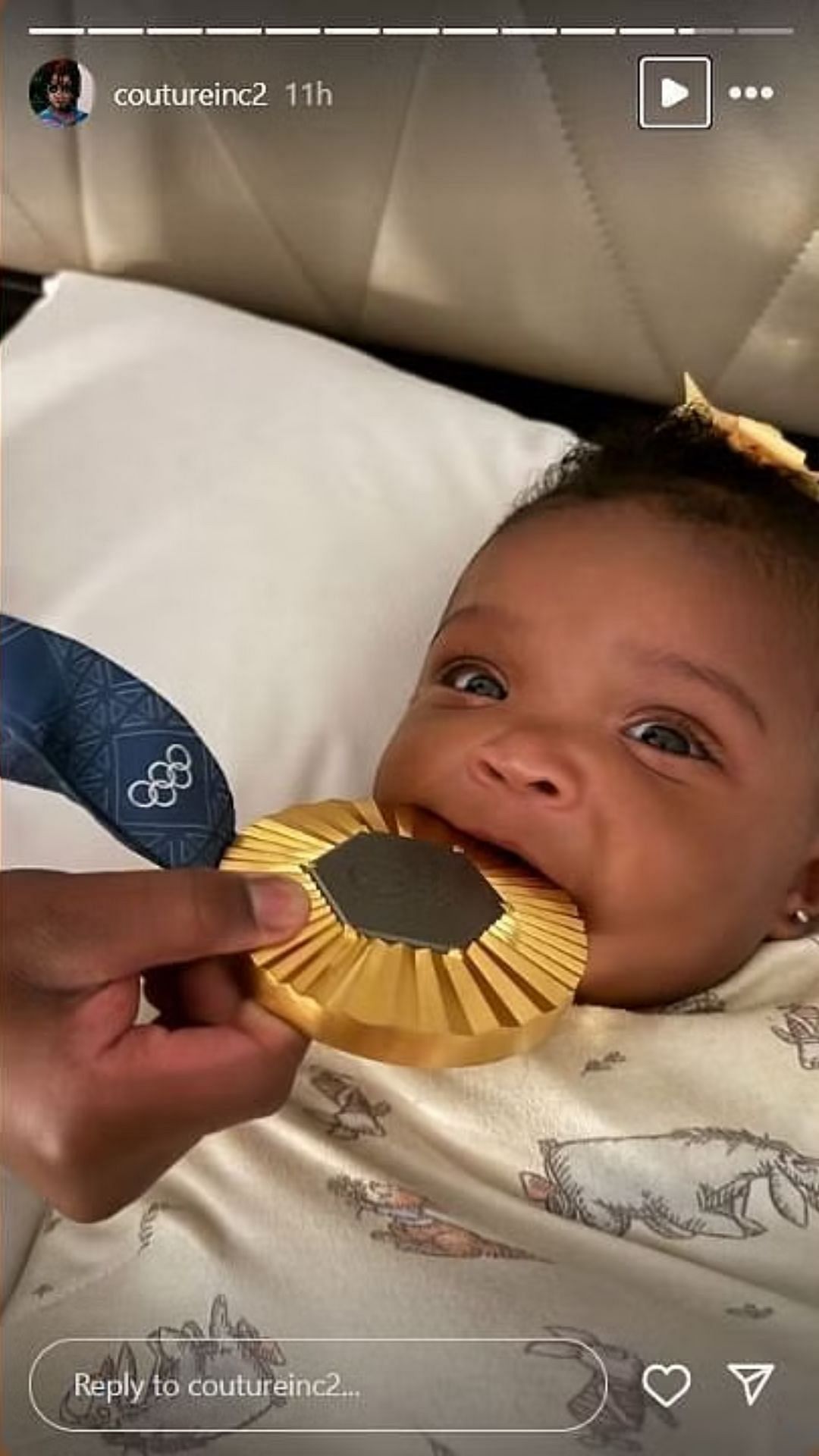 Edwards and Robel's daughter Aislynn biting on the gold medal. (Credits: @coutureinc2/Instagram)