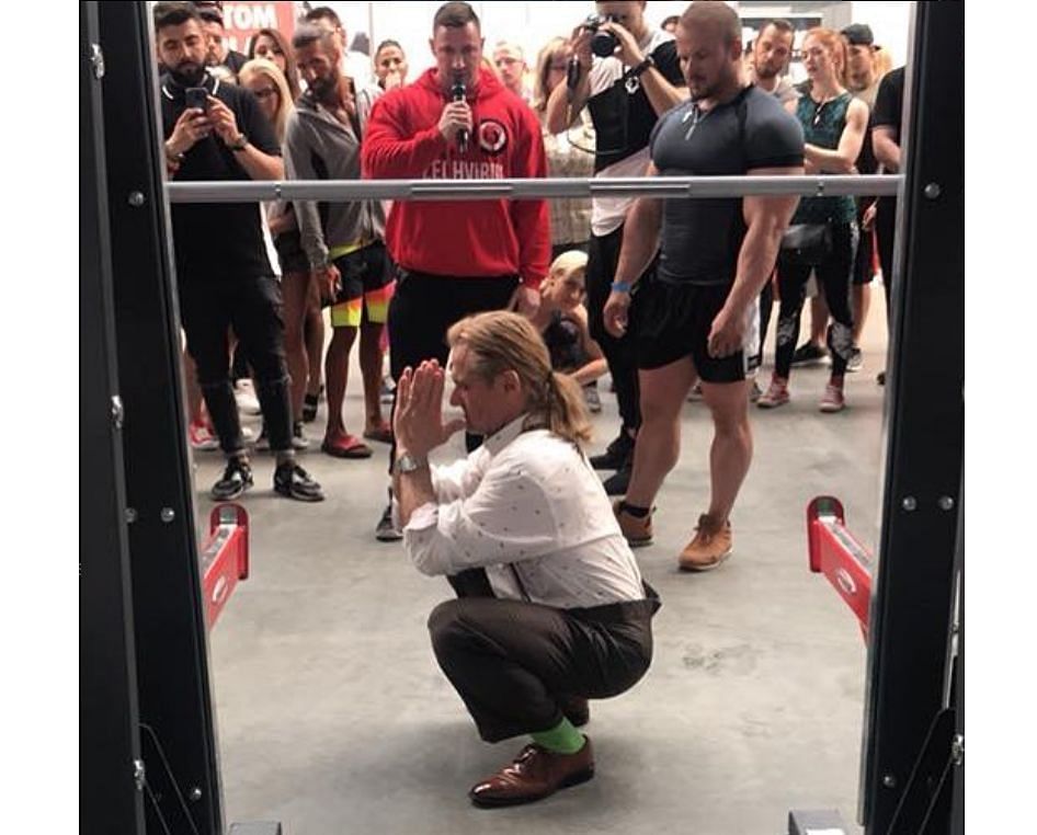 Tom Platz squatting with joined hands, in the squatting rack p.c.: @tomplatz on Instagram