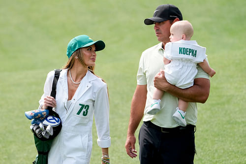 American professional golfer Brooks Koepka carries his son, Crew, while walking near the no. 4 green with his wife, Jena Sims, during the Par 3 Contest at Augusta National Golf Club during the 2024 Masters [Image via Imagn]