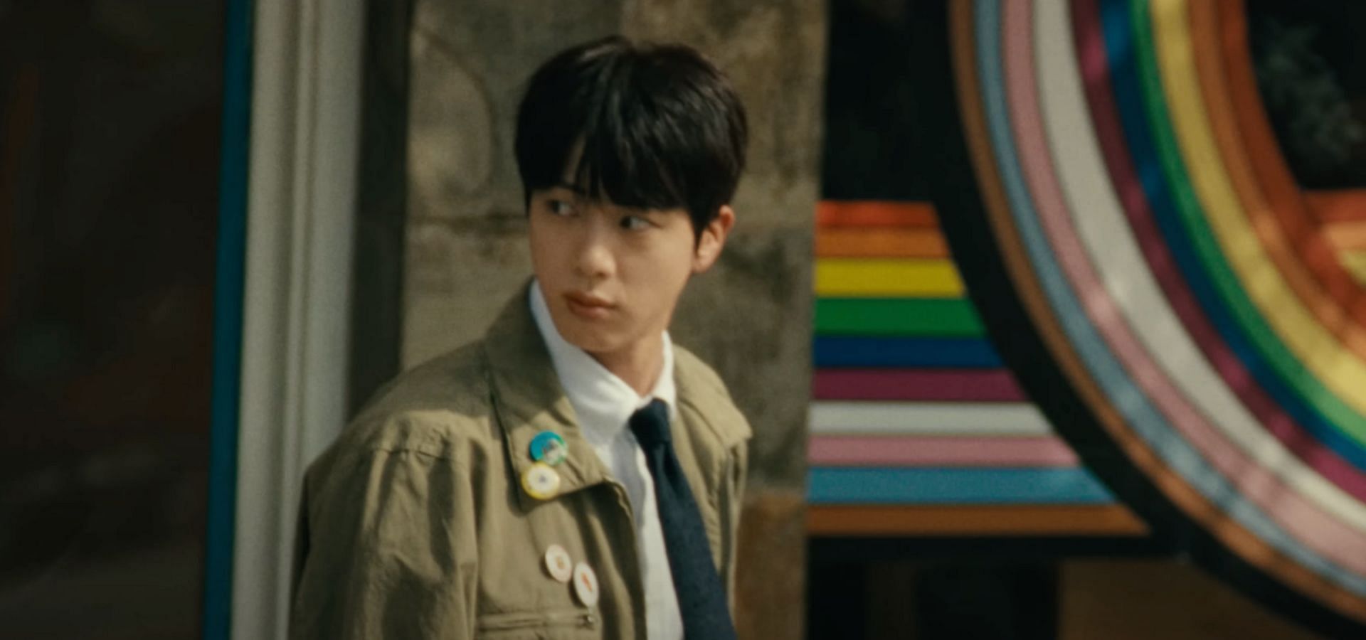 The BTS idol standing in front of the pride flag. (Image via YouTube/HYBE LABELS)