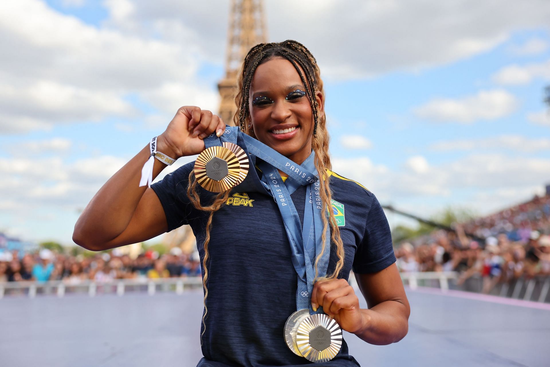 Andrade in a blue t-shirt posing with her medals at the Champions Park on the 12th day of the 2024 Paris Olympics (Image via: Getty Images)