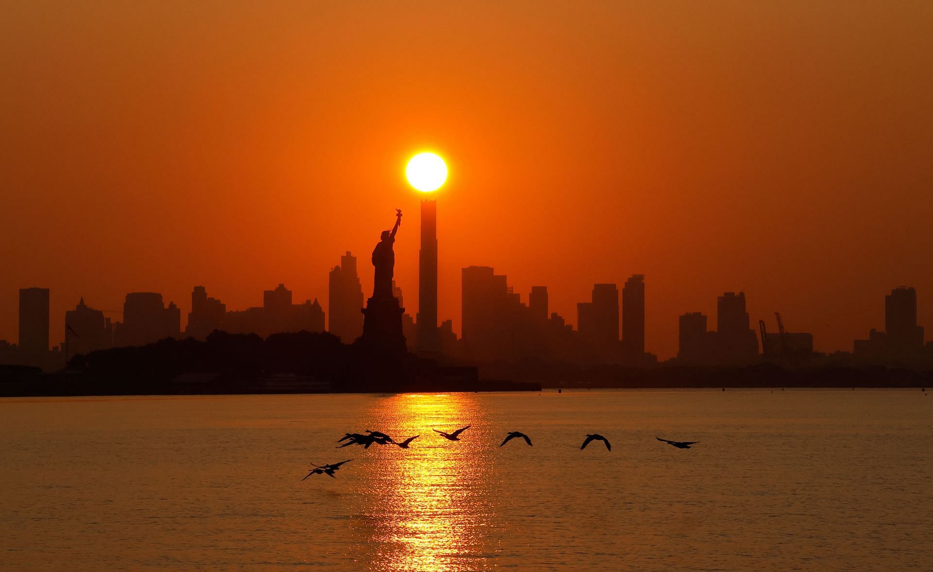 Sunrise Behind the Statue of Liberty in New York City (Image via Getty)