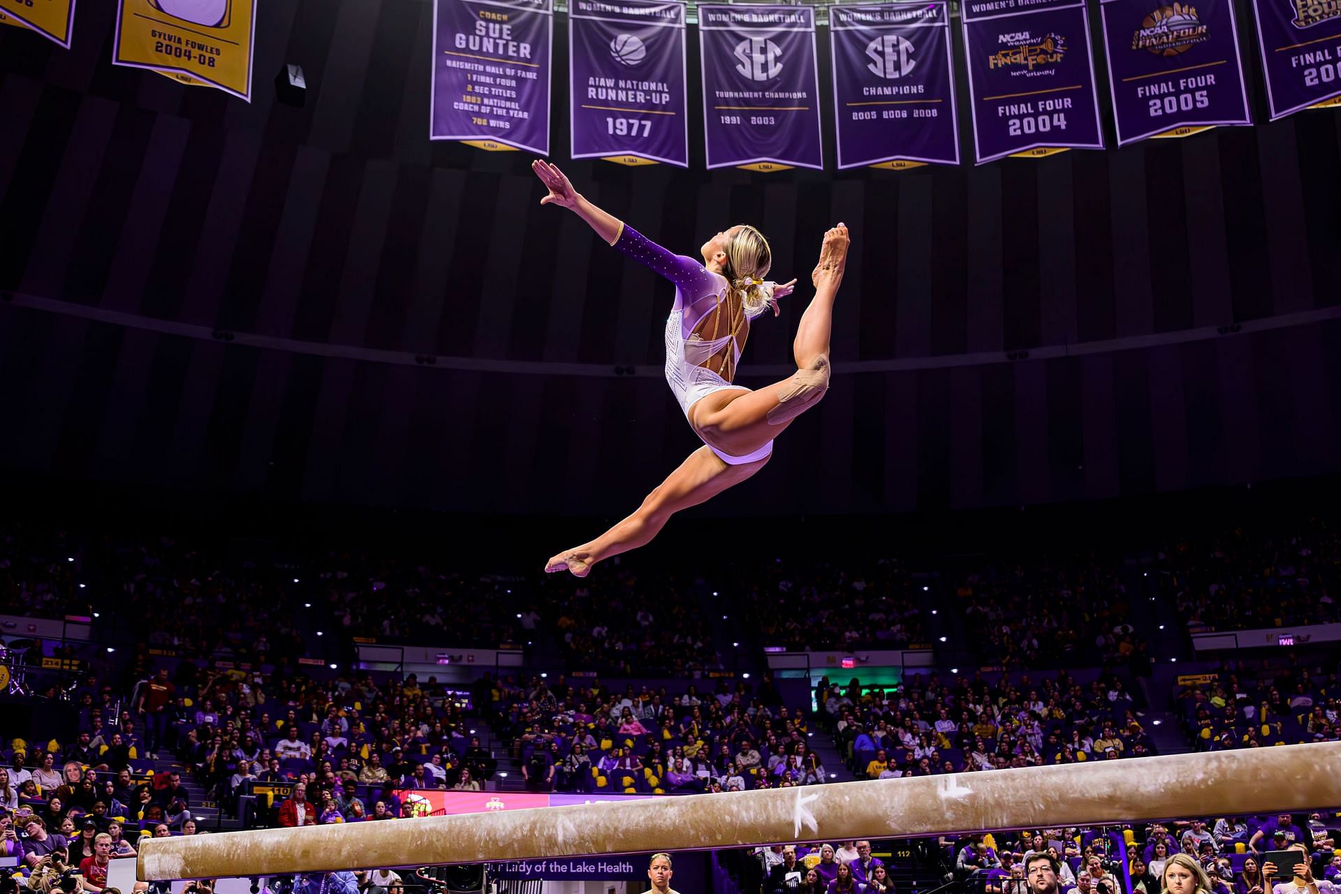 Olivia Dunne performing her beam balance routine in a purple and white leotard during the meet against IOWA State (Image via: Getty Images)