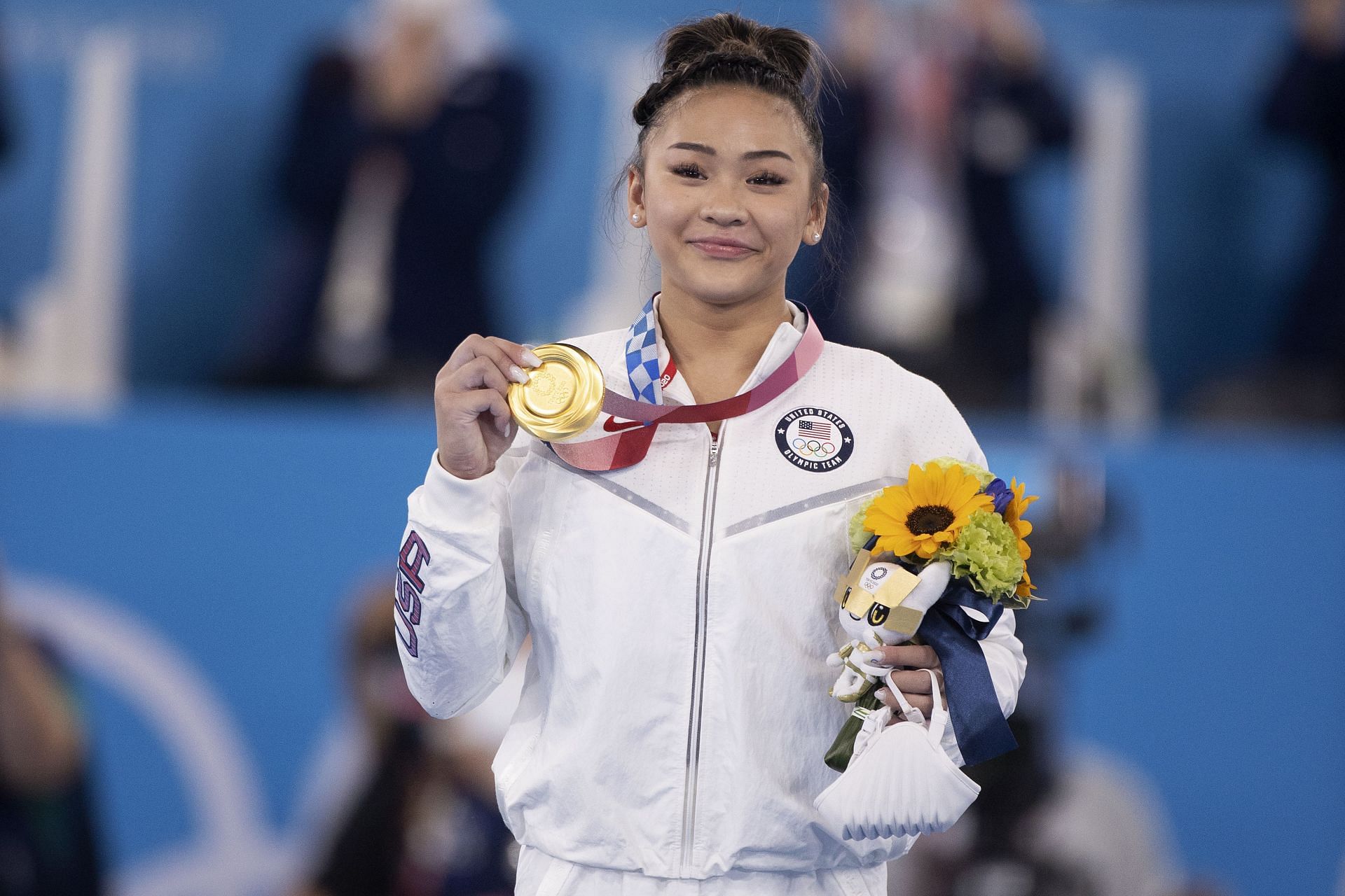 Suni Lee celebrating with her all-around gold medal on the podium during the delayed 2020 Tokyo Olympics (Image via: Getty Images)