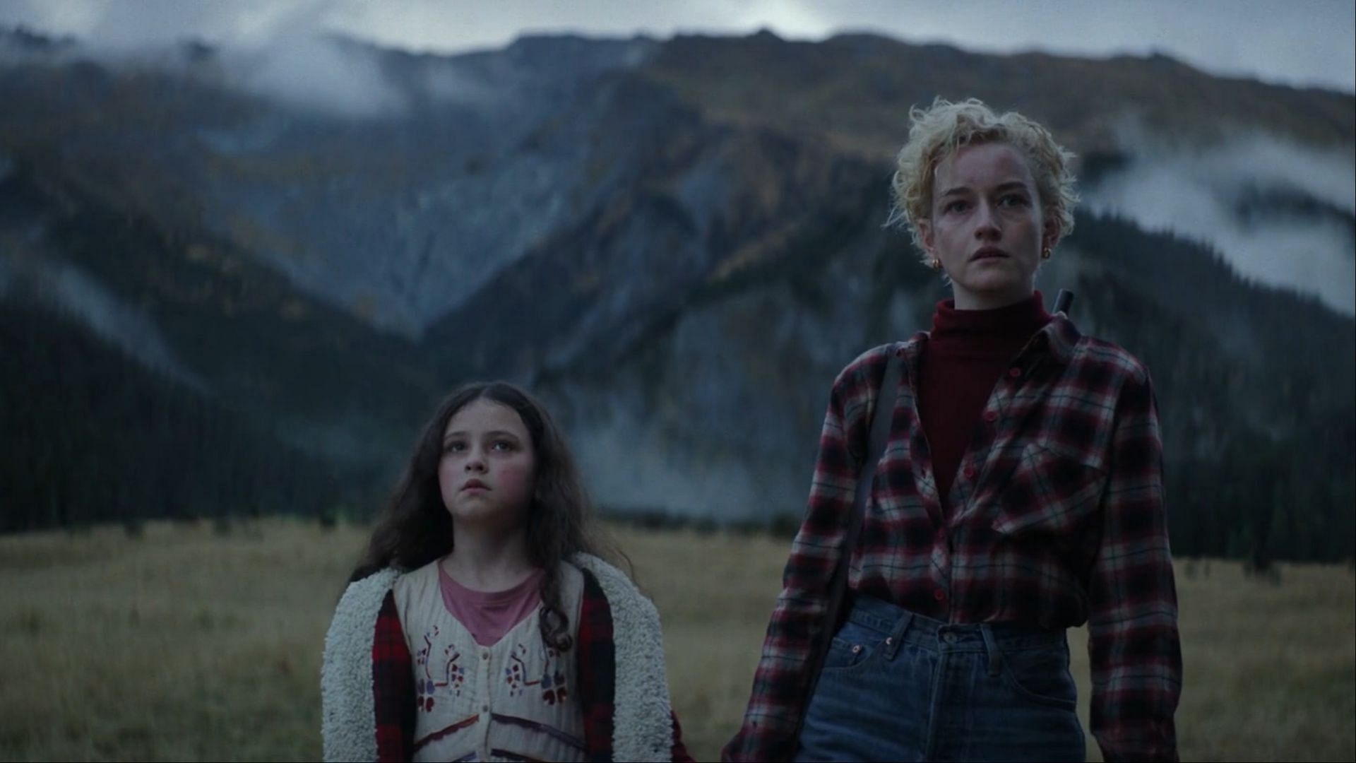  In the climactic final scene of Wolf Man, Julia Garner as Charlotte and Matilda Firth as Ginger stand against a haunting mountainous backdrop. (Image via AppleTv+) 