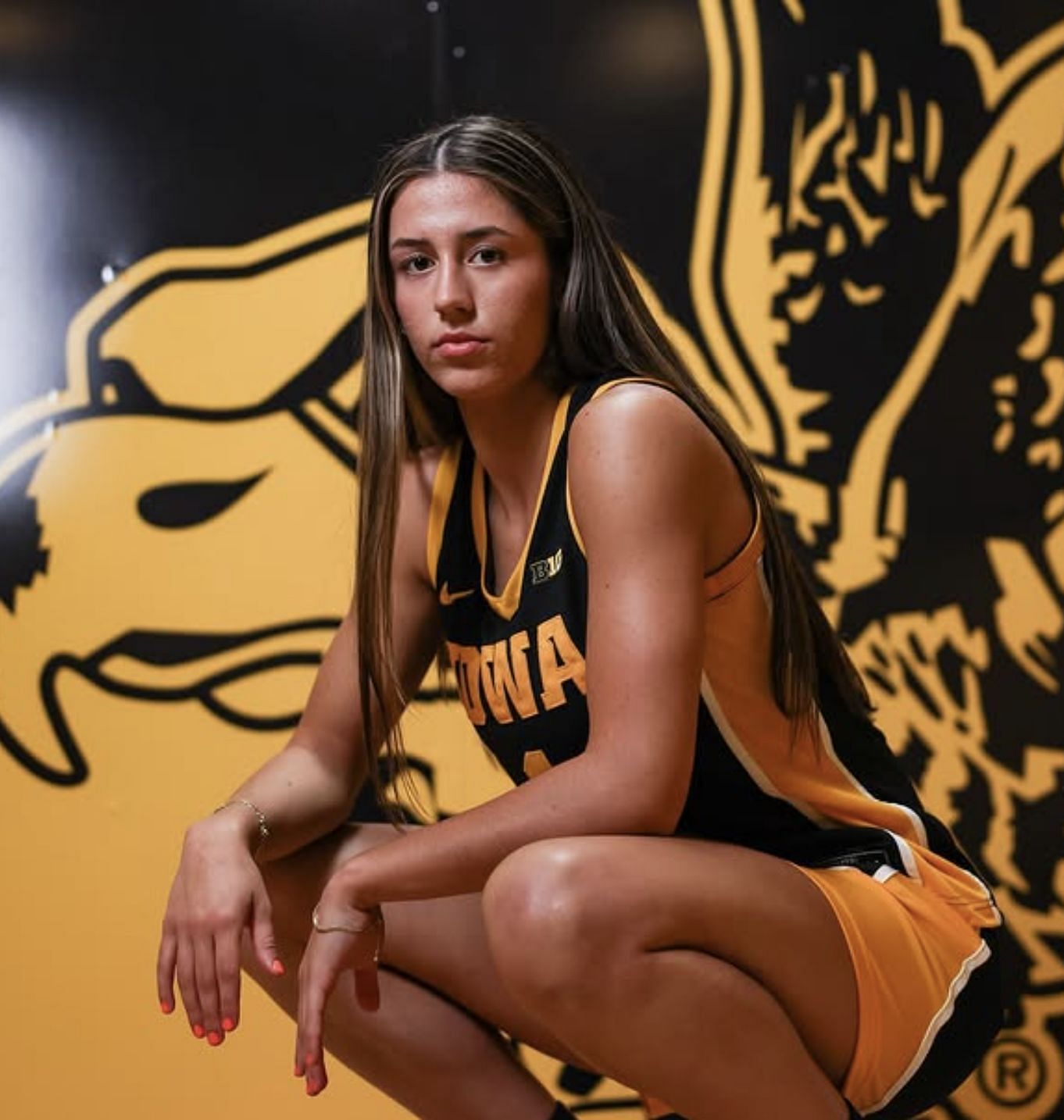 Addie Deal poses in an Iowa Hawkeyes basketball uniform against a bold black and gold Hawkeye backdrop, showcasing her commitment to the program.