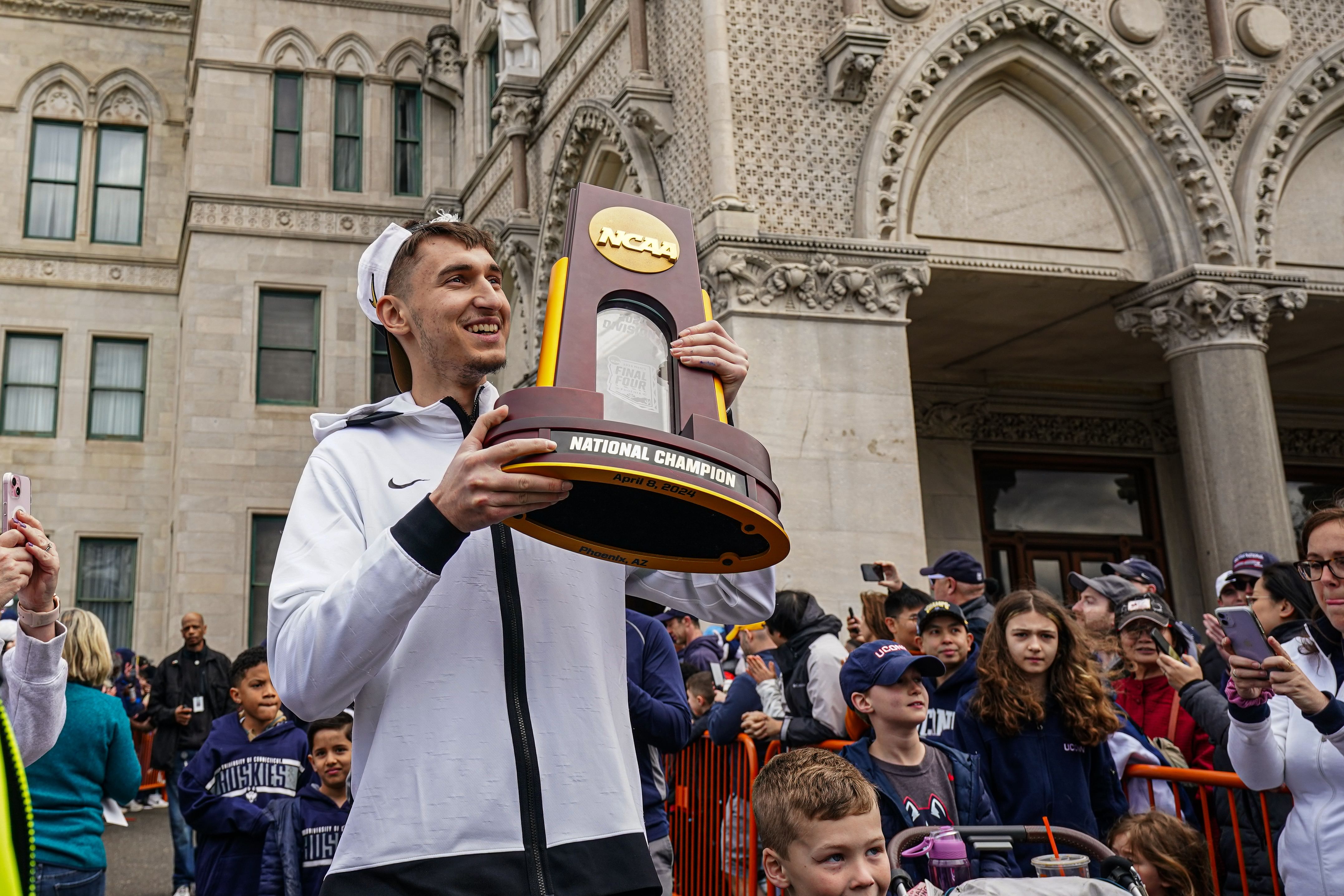 UConn Huskies guard Apostolos Roumoglou (#33) holds the NCAA Championship trophy as he and his teammates leave the State Capitol to start their victory parade. Photo: Imagn