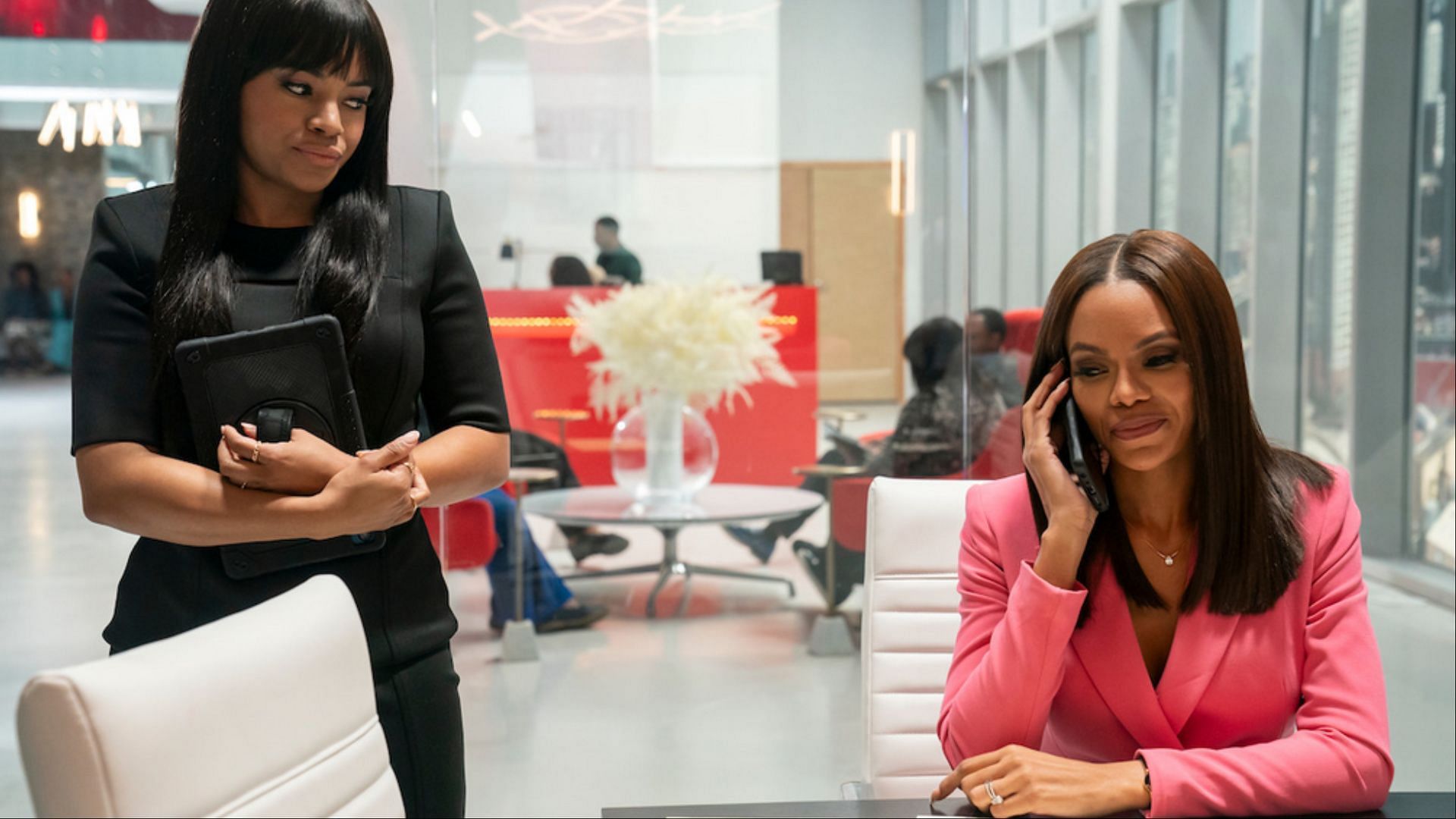 Taylor Polidore Williams as Kimmie (left) and Crystle Stewart as Mallory Bellarie (right) &ndash; Kimmie stands in a corporate office holding a tablet, observing Mallory, who is engaged in a phone conversation. (Image via Netflix Tudum)