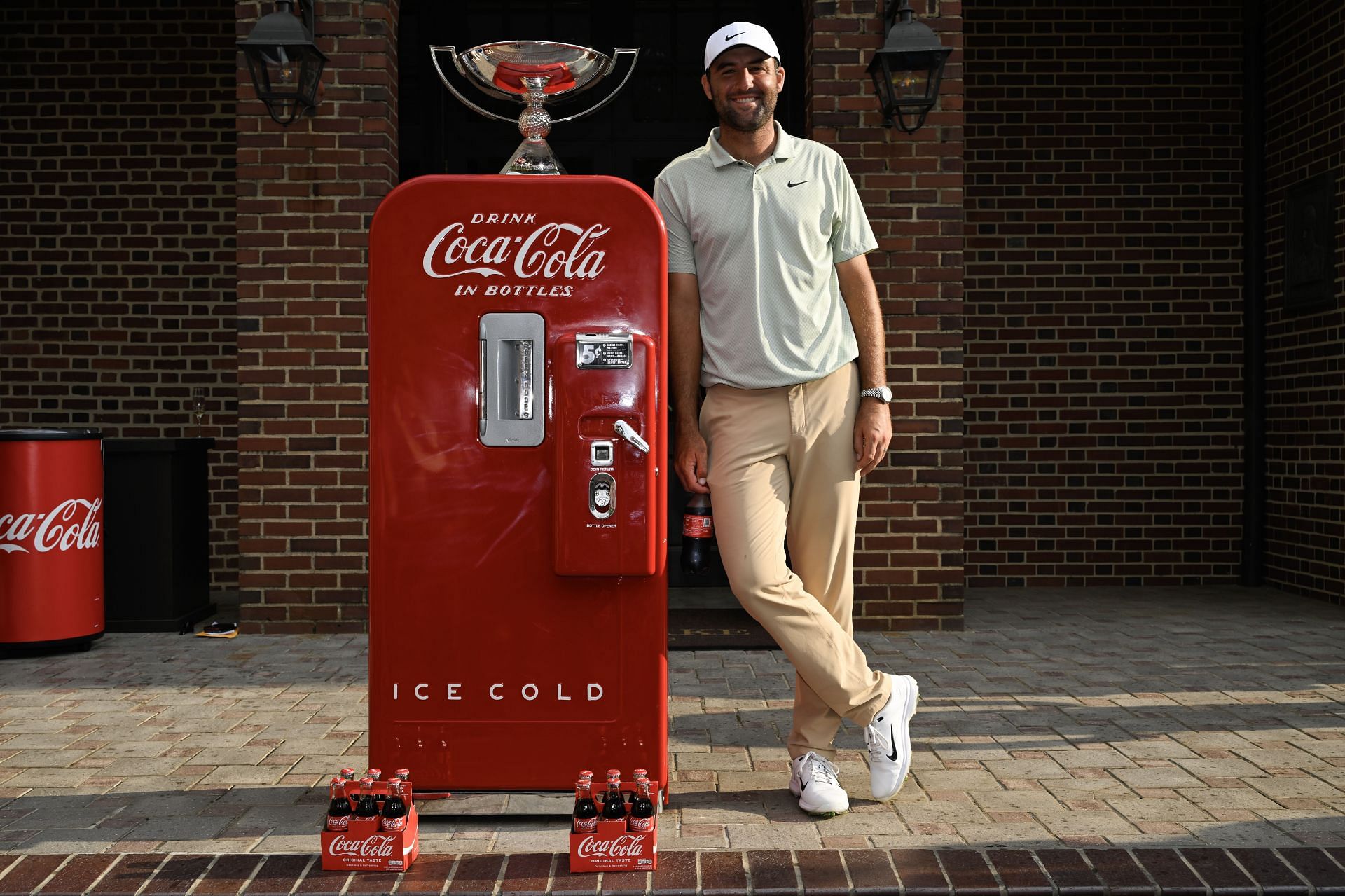 Scottie Scheffler posing with the FedEx Cup trophy and the Coca-Cola vending machine after winning the 2024 Tour Championship (Source: Getty)