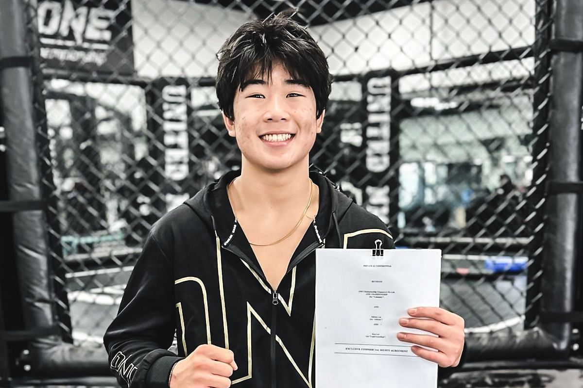 Adrian Lee smiles at the camera, holding his contract