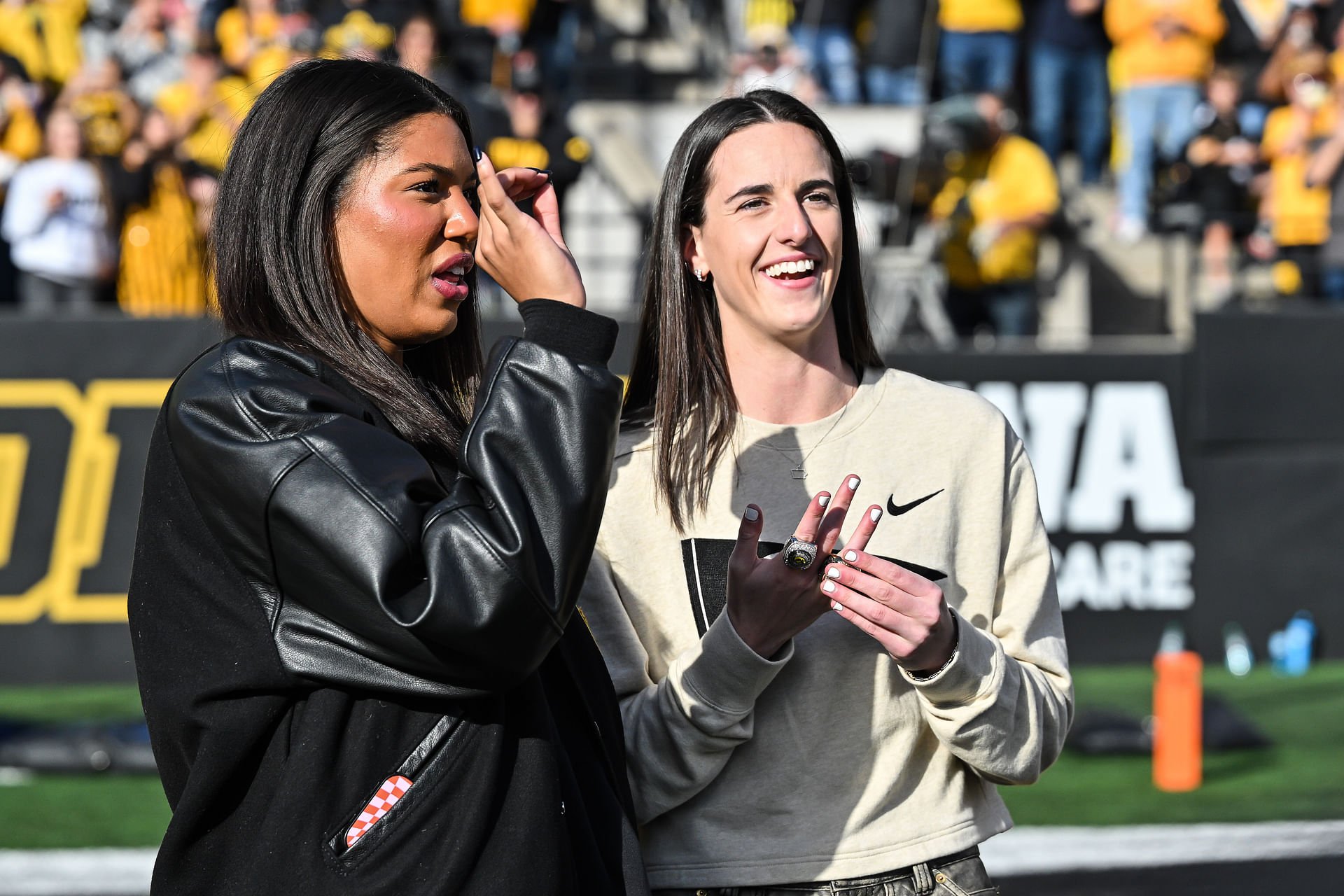 Oct 26, 2024; Iowa City, Iowa, USA; Former Iowa Hawkeye and current Indiana Fever WNBA star Caitlin Clark (right) and current Hawkeye basketball player Jada Gyamfi (left) look on while being honored during the game between the Iowa Hawkeyes and the Northwestern Wildcats at Kinnick Stadium. Mandatory Credit: Jeffrey Becker-Imagn Images - Source: Imagn