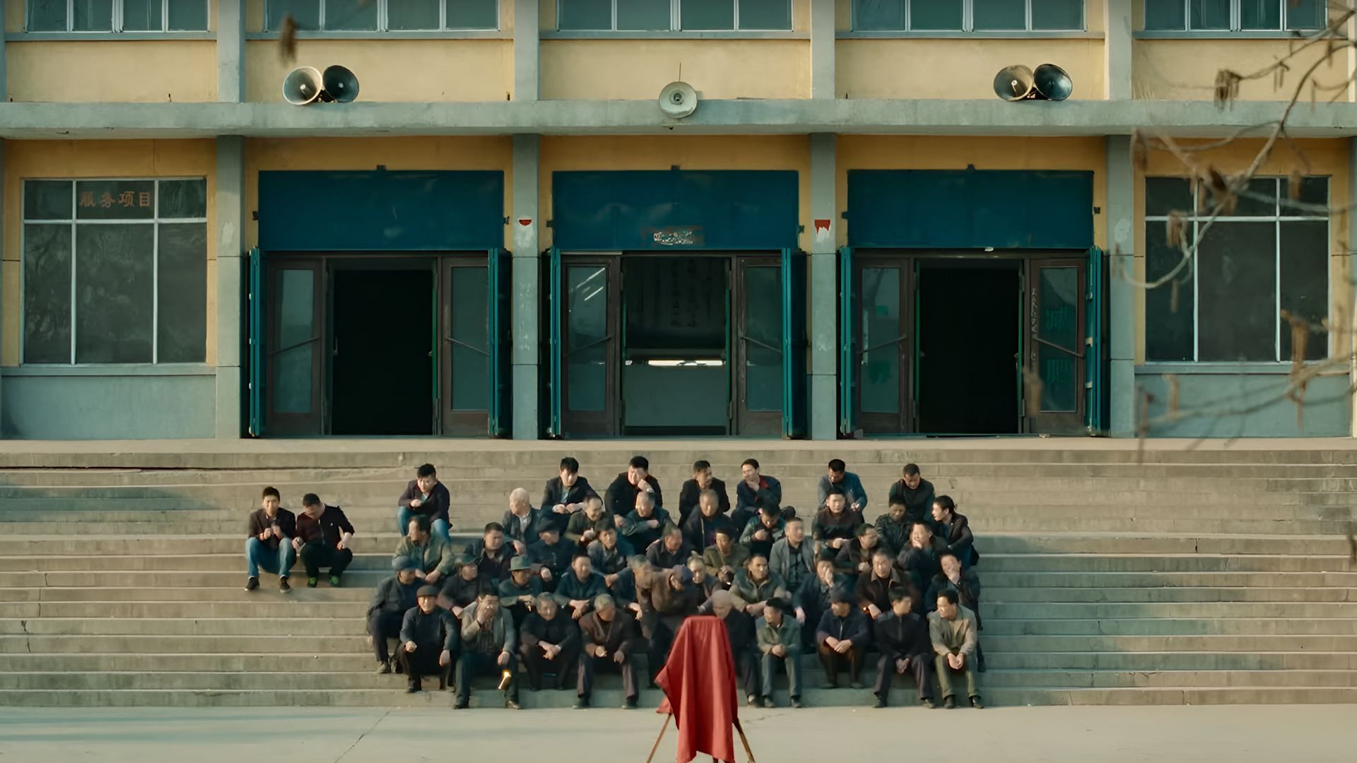 A still from Caught by the Tides showing a solemn gathering of workers outside an industrial building in northern China. (Image via Janus Films)