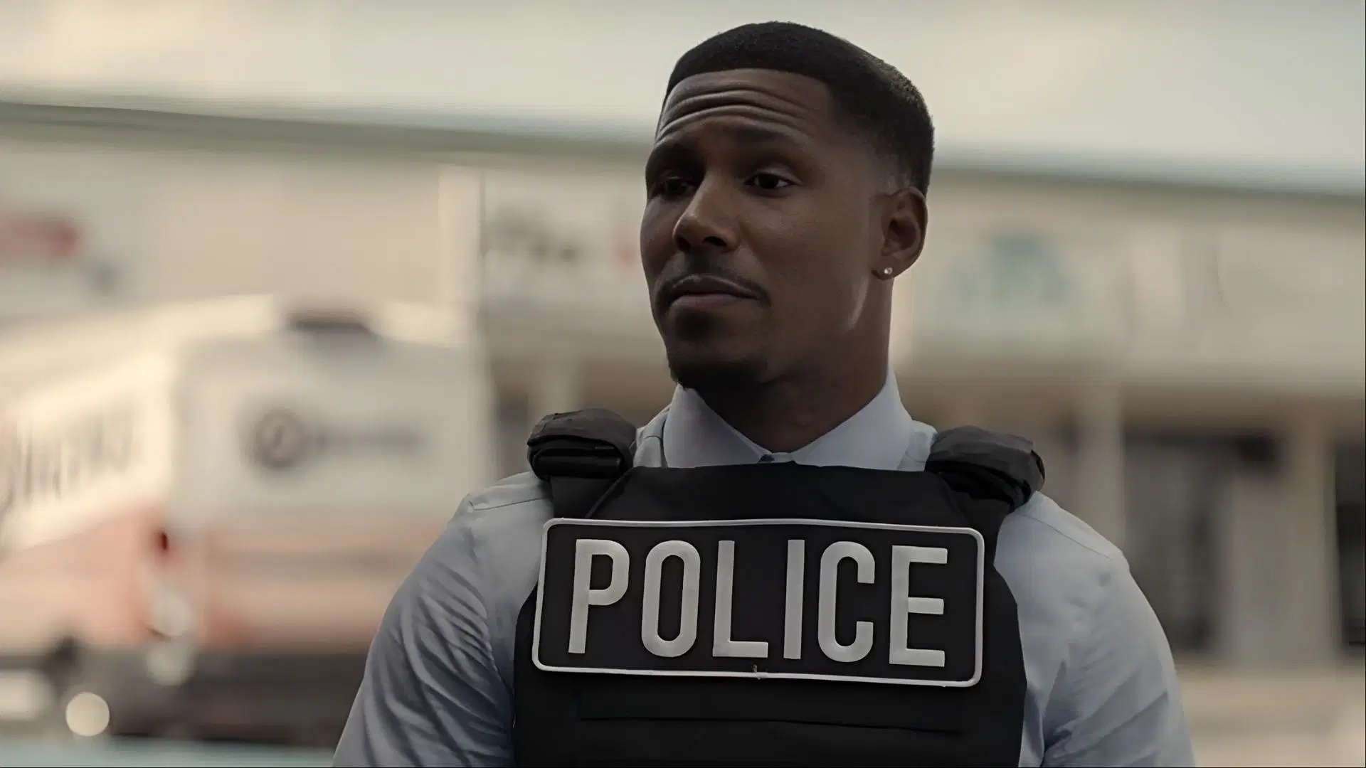 Mike Merrill as Detective Grimes, dressed in a light shirt and bulletproof vest marked &ldquo;POLICE,&rdquo; assessing the scene outside the bank.