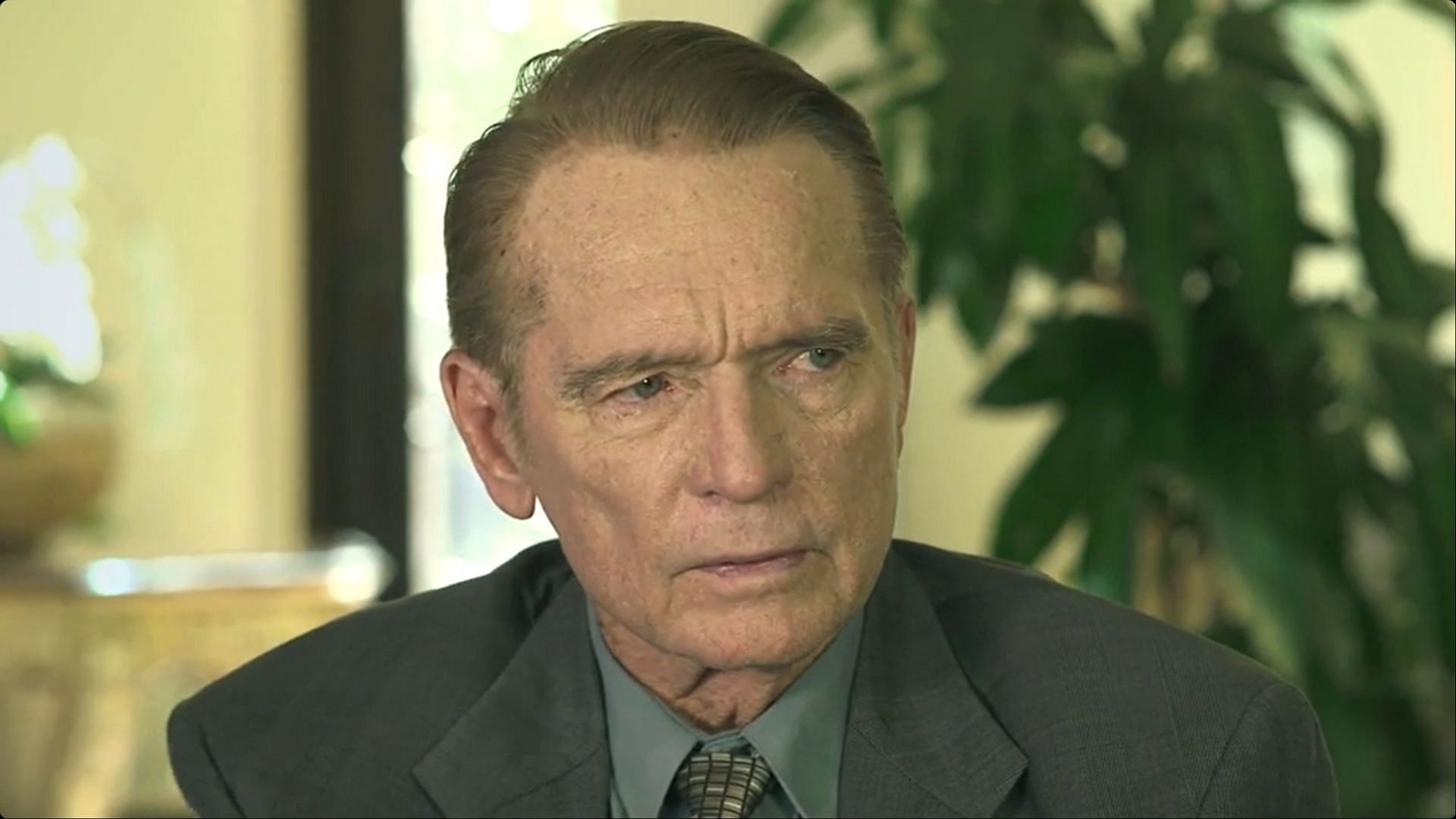Chris Robinson in a suit seated indoors with a serious expression.